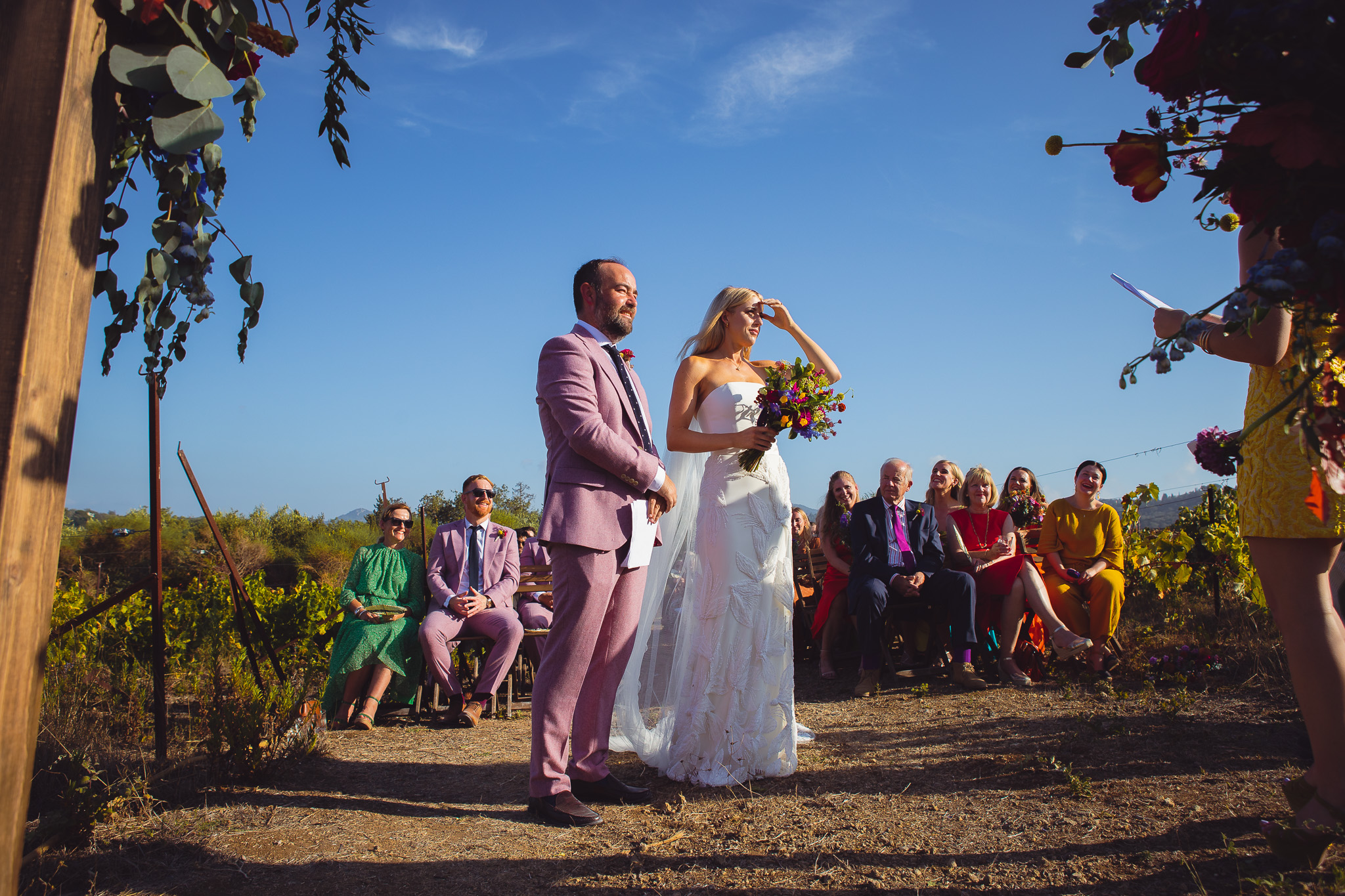 The bride and groom stand in front of their guests at their sunny wedding reception at their destination wedding