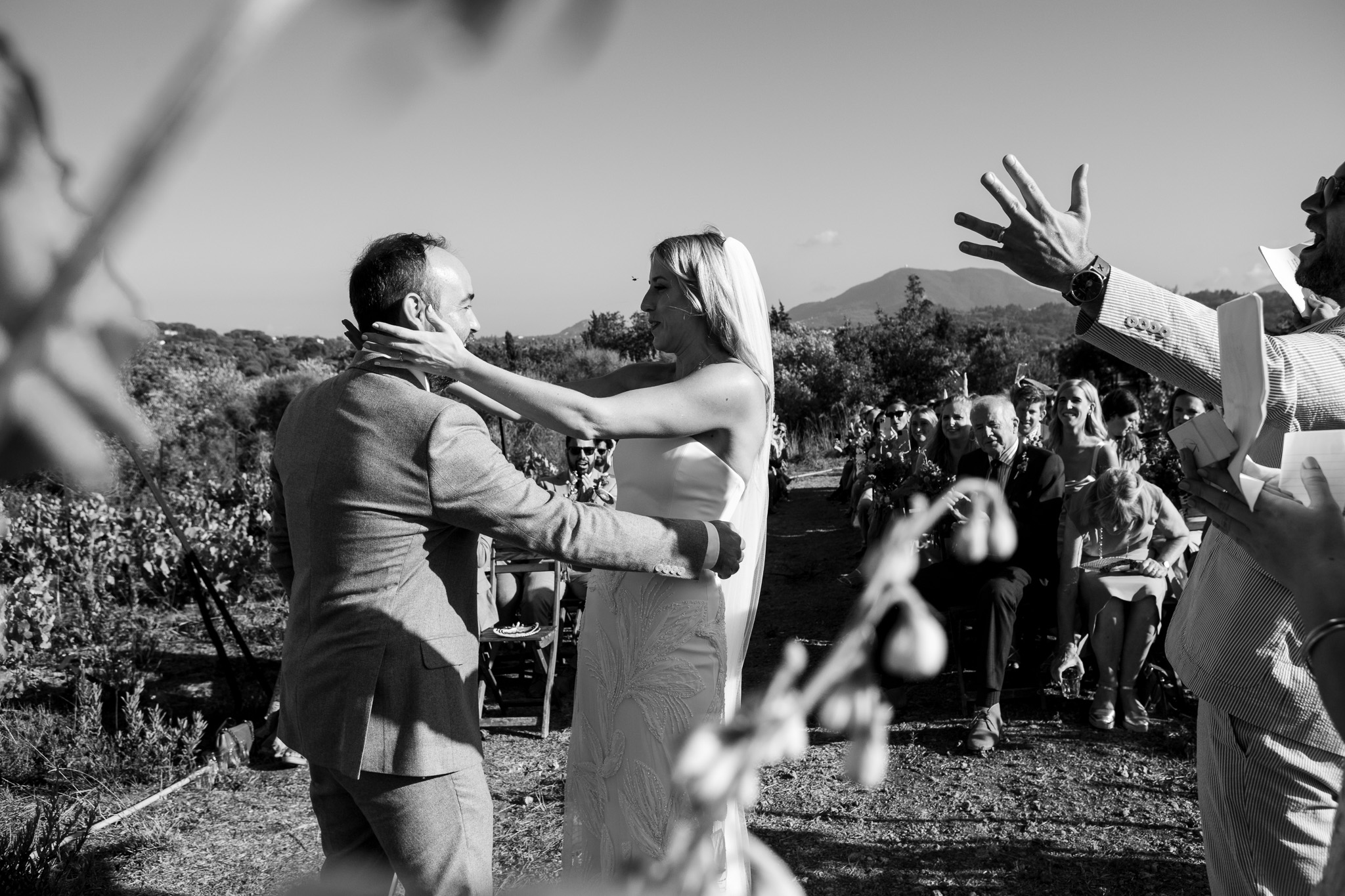 The celebrant holds out his arms whilst the bride and groom go in for an embrace during their wedding ceremony