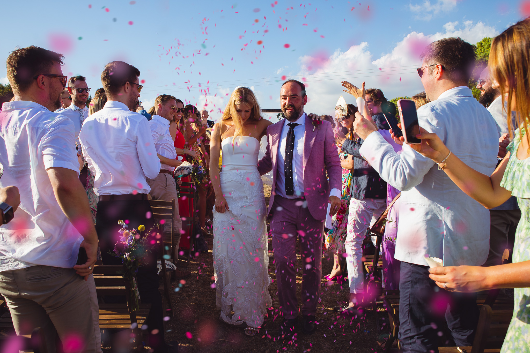 The bride and groom walk through their guests and pink confetti at their wedding ceremony