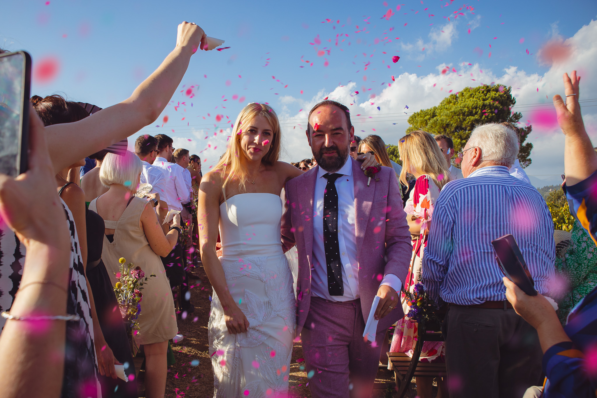 Guests throw pink confetti at the bride and groom who are walking down the aisle at the wedding ceremony