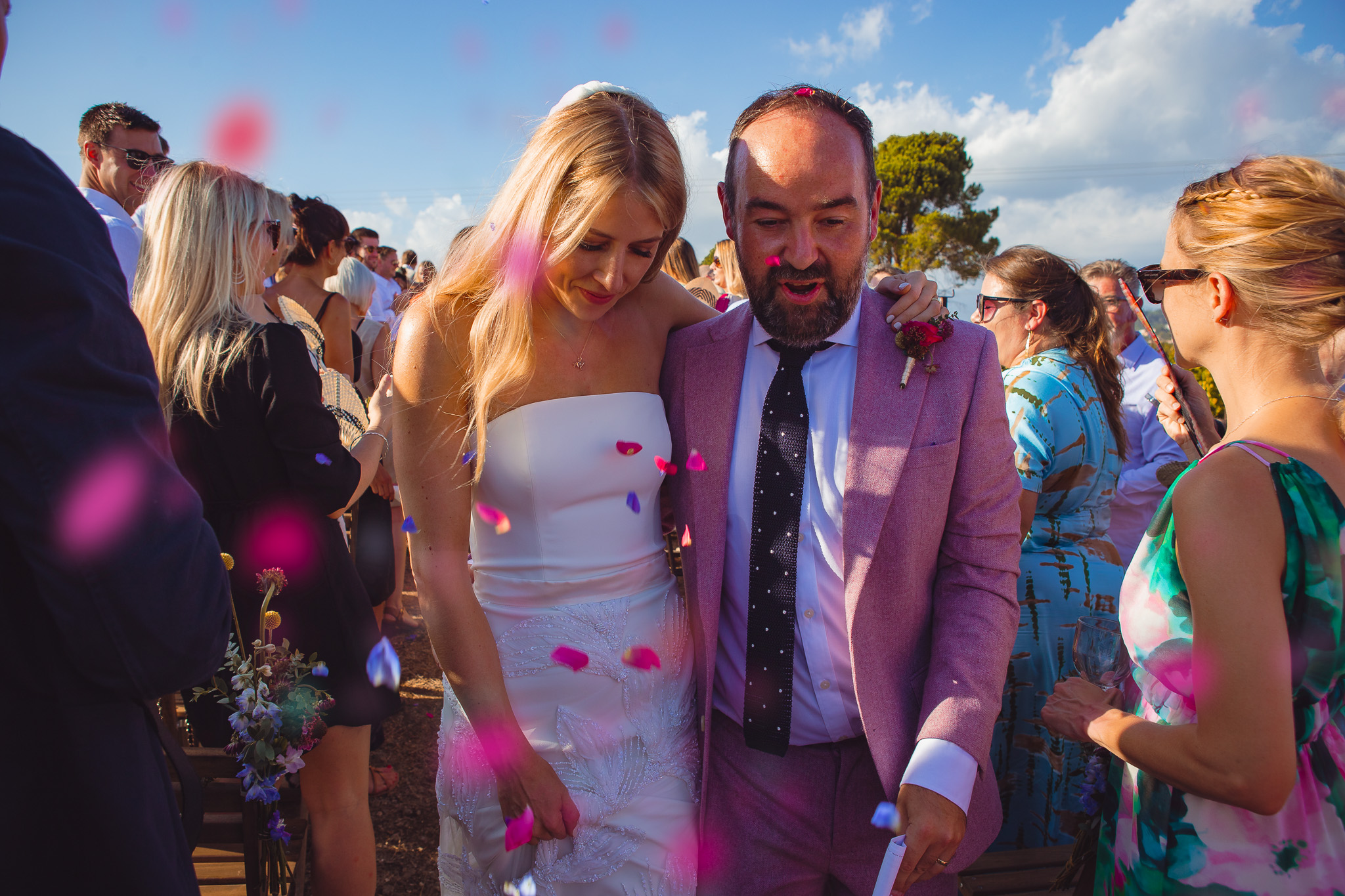 Bride and groom walk through pink confetti and their guests at the end of their wedding ceremony