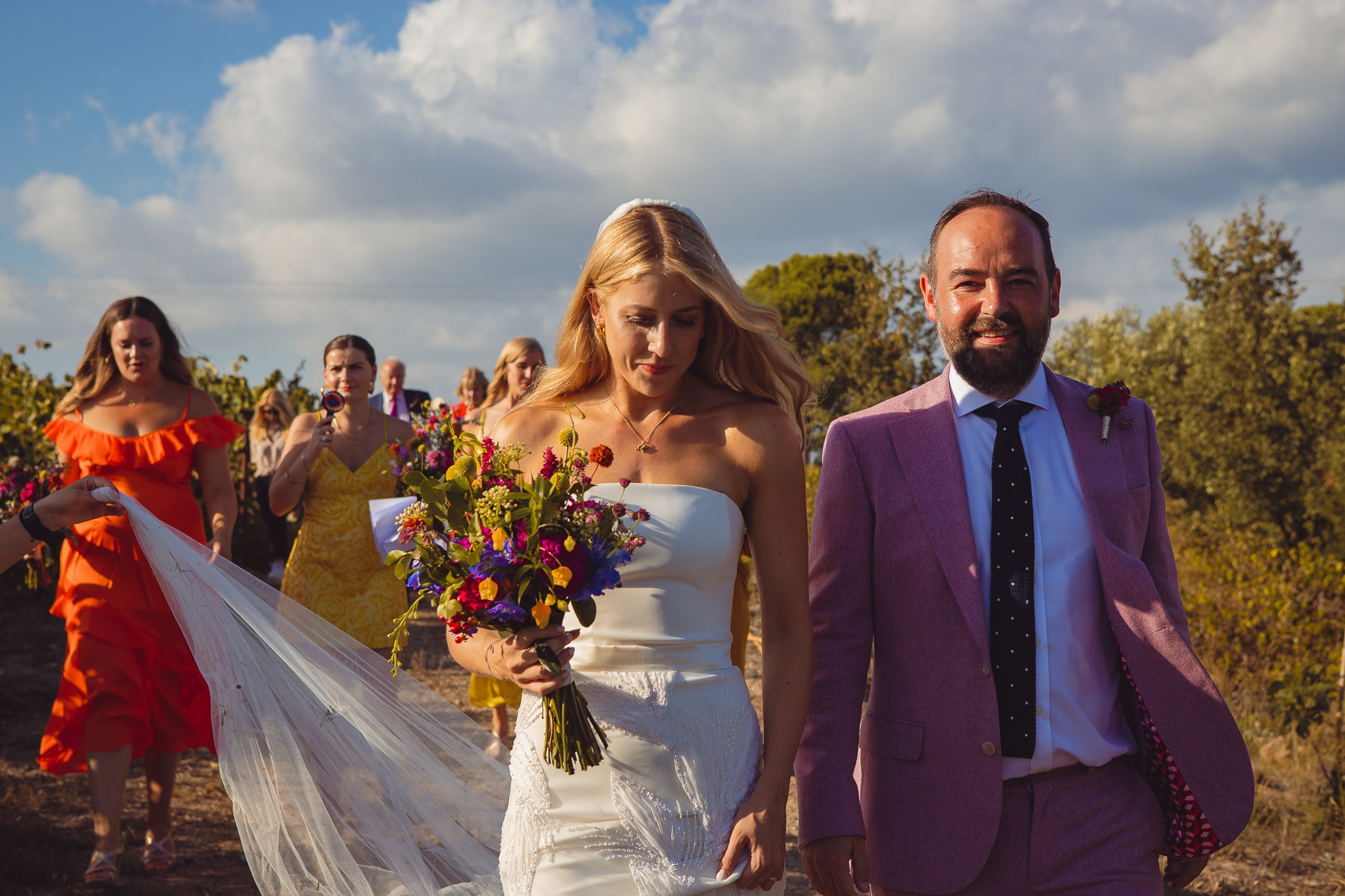 The bride and groom walk together followed by bridesmaids after their wedding ceremony at Ambelonas Vineyard, Corfu