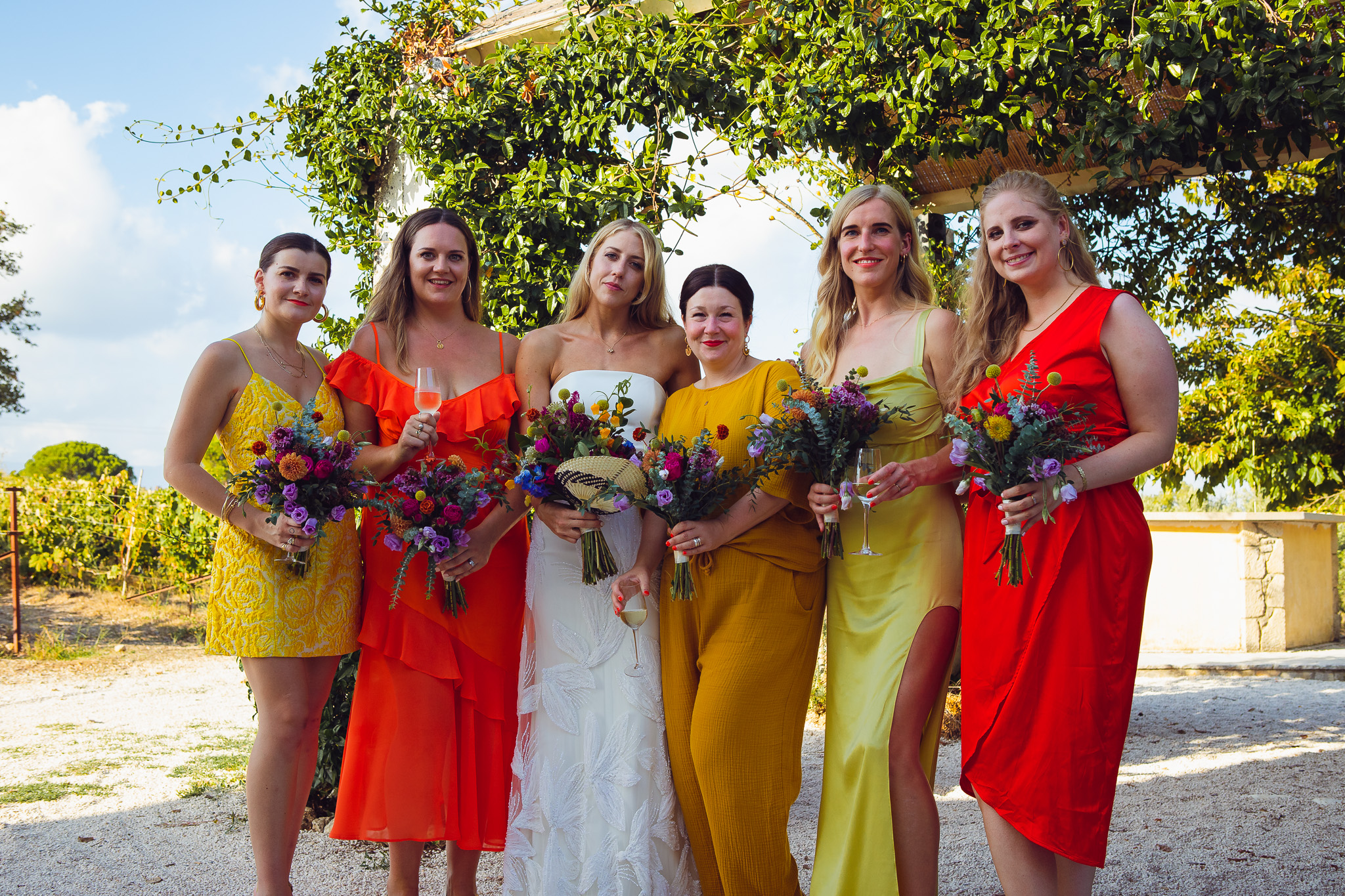 The bride and five brightly dressed bridesmaids stand together and pose for a group shot