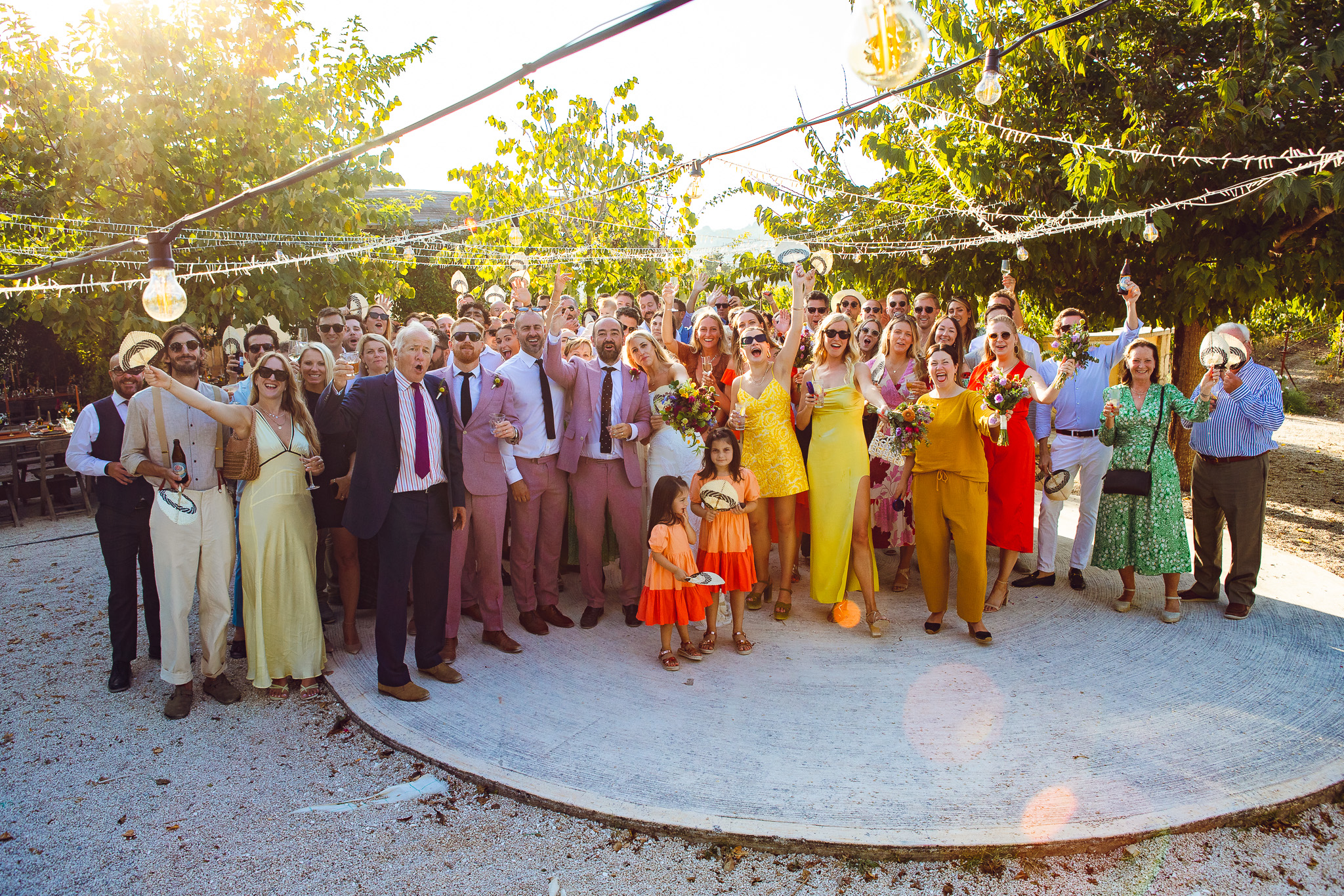 A large group shot of all the wedding guests shouting in the sunny Ambelonas Vineyard, Corfu