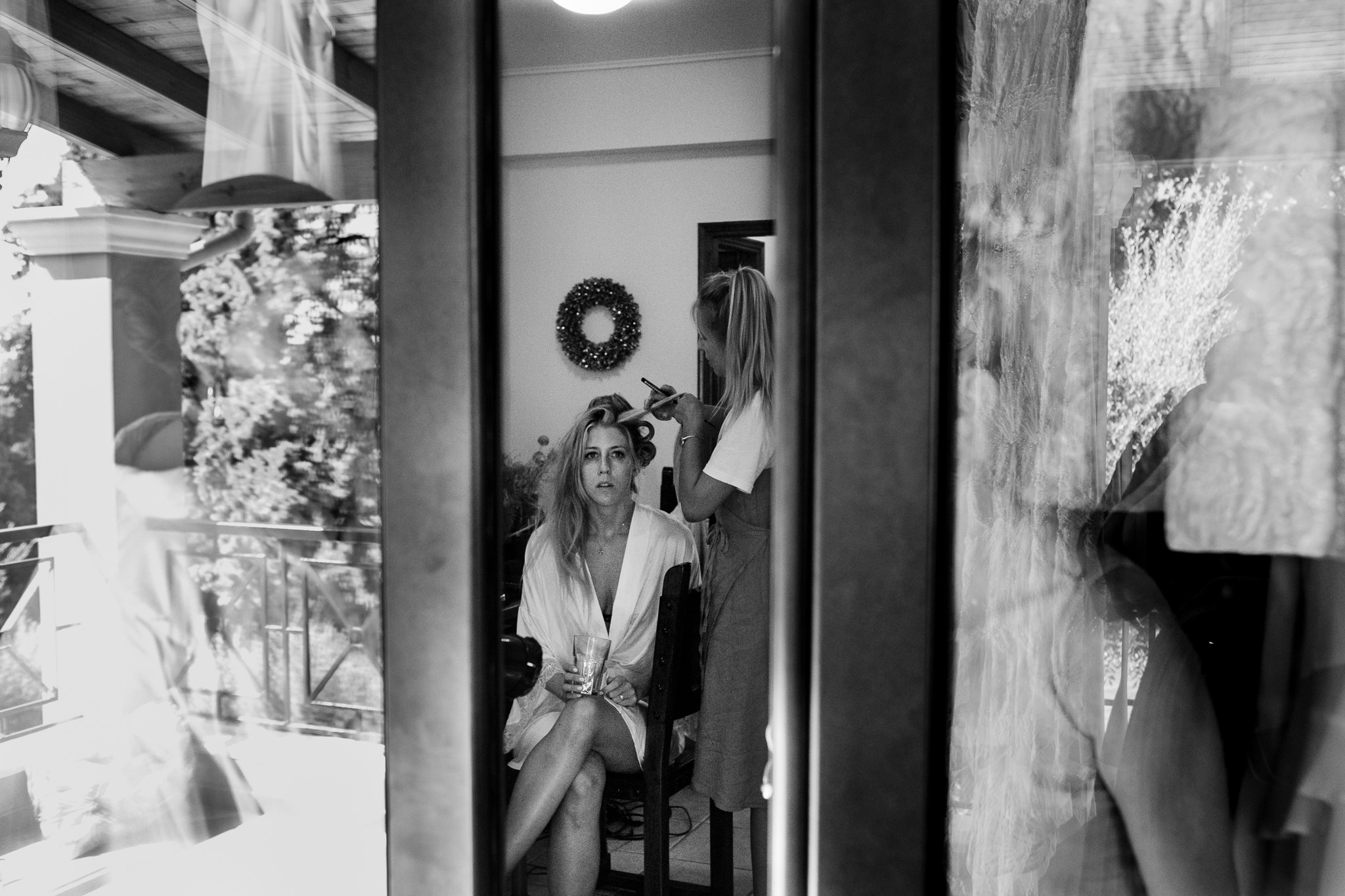 Alice getting her wedding hair and make-up finished whilst she looks out through a window of her Crete villa.