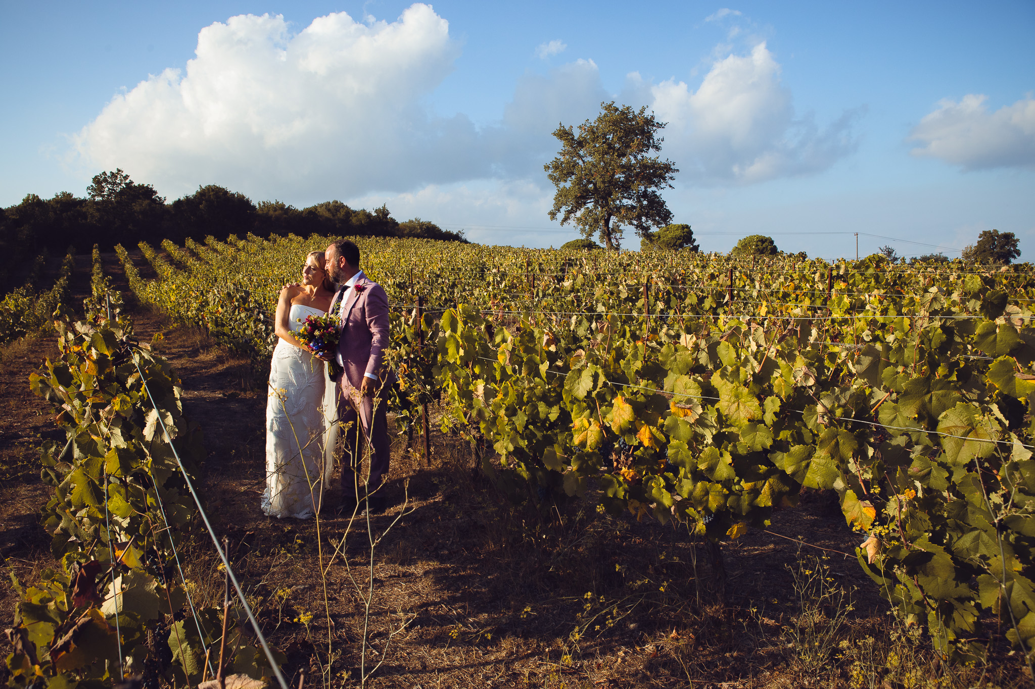 Alice and Tom stand together in the vineyard and pose for a couples portrait at their destination wedding