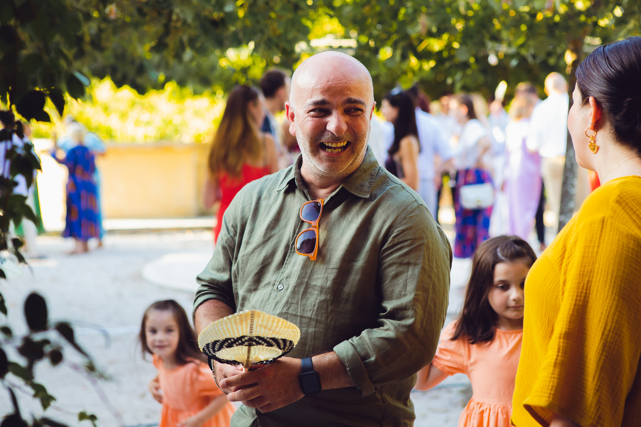 A wedding guests laughs as he fans himself in the Corfu heat at the wedding reception