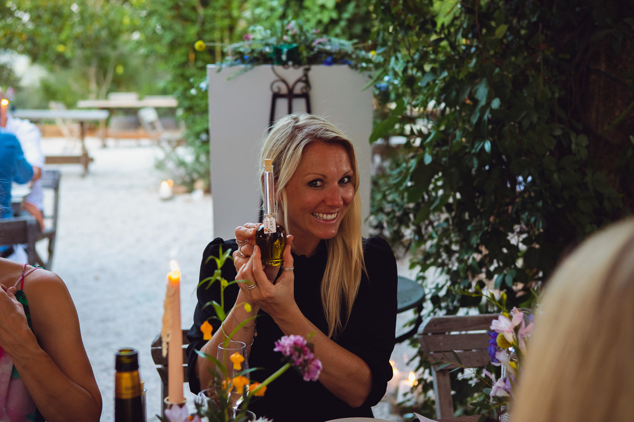 Guest holds up and poses with mini olive oil bottle at the wedding dinner table
