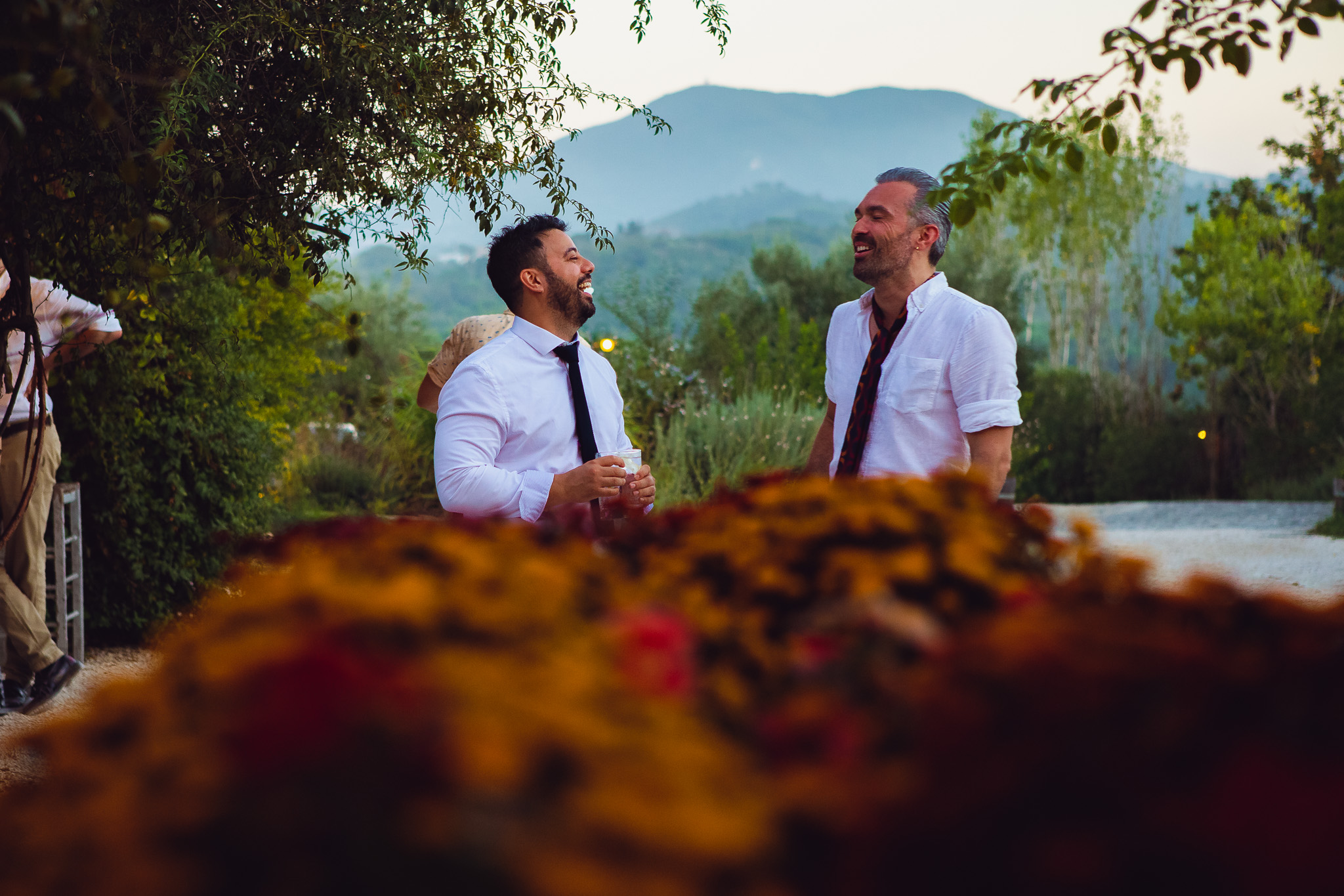 Two guests laugh and chat at a stunning destination wedding at Ambelonas Vineyard, Corfu