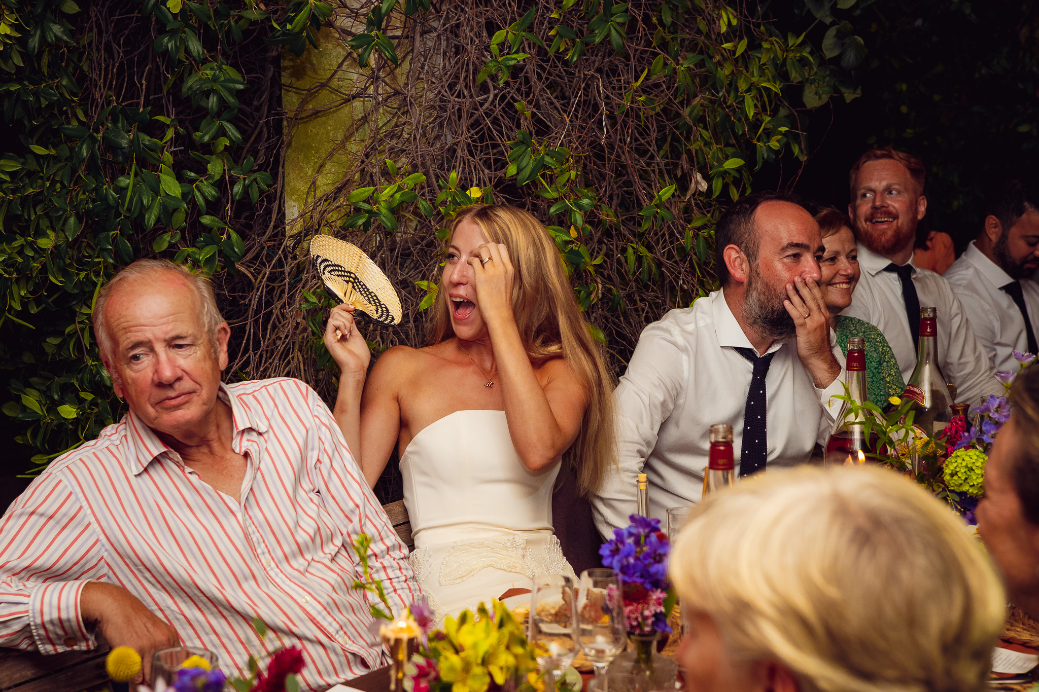 Bride, groom and guests laugh as they listen to a speech during their wedding dinner