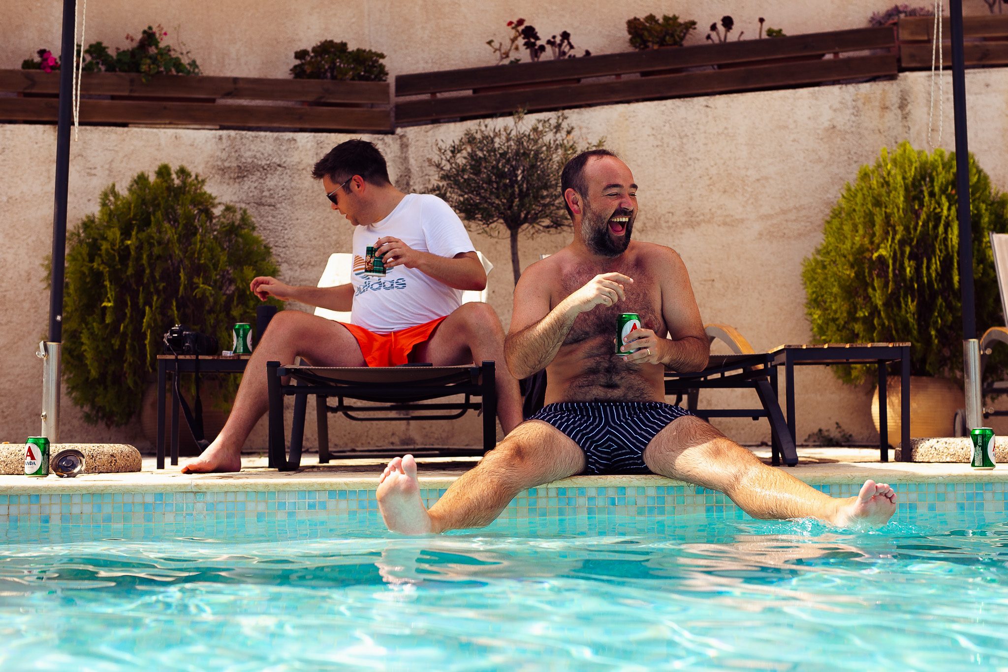 The groom laughing as he sits on the edge of the pool at his villa in Crete before getting ready for his wedding.