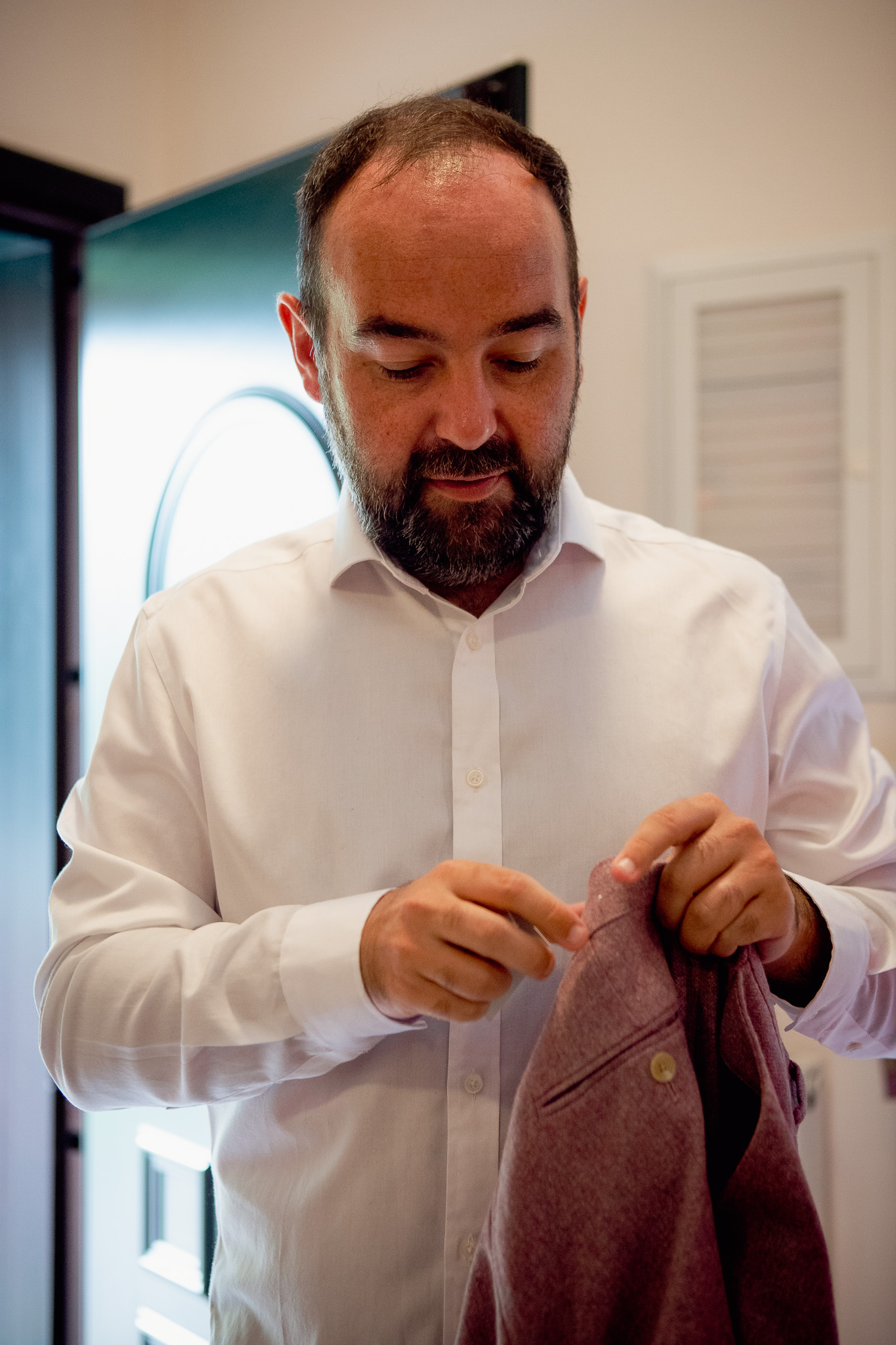 Groom getting dressed whilst looking at the suit that he's holding.