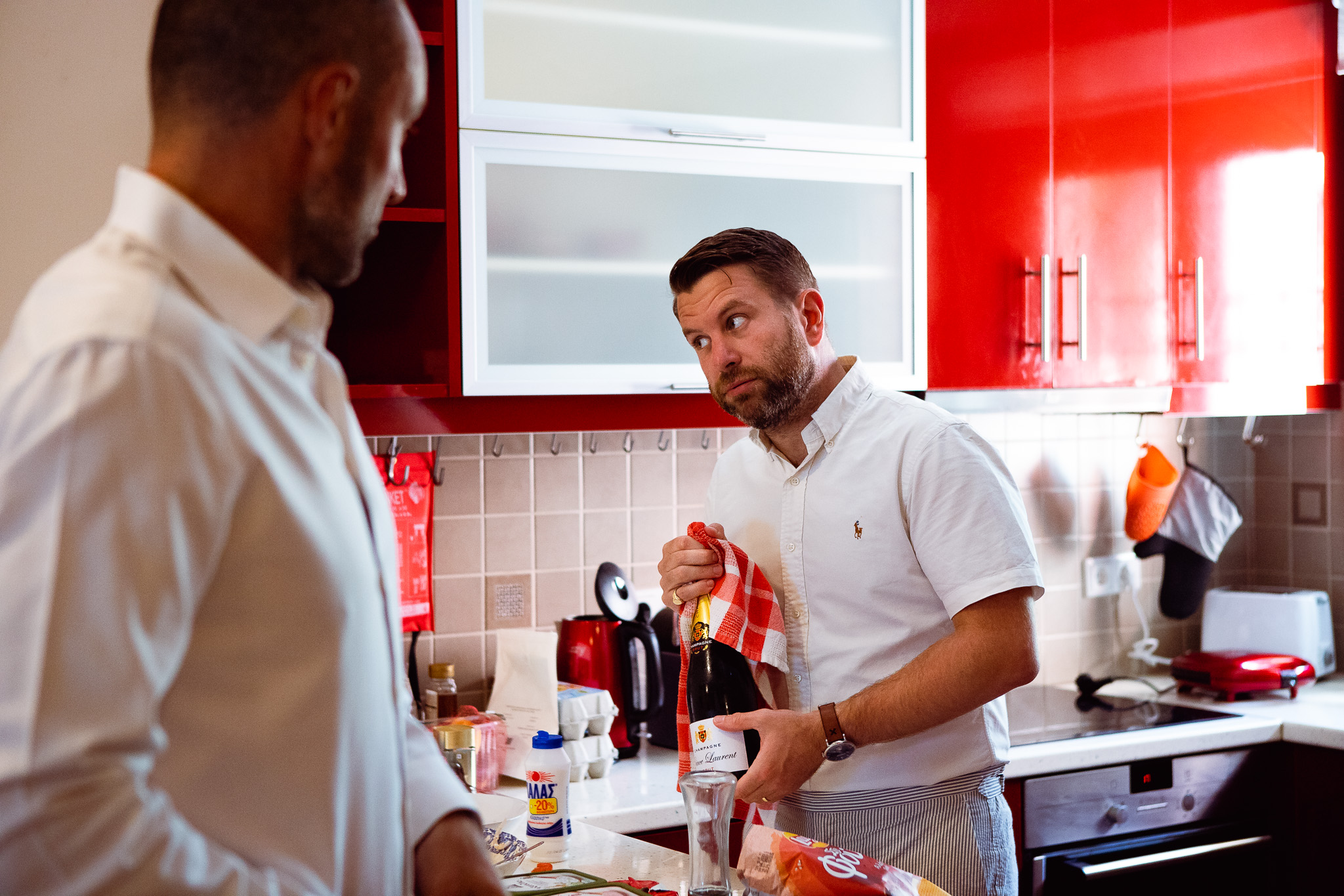 Groomsman holding out a bottle of champagne in the kitchen before heading to his friend's wedding.