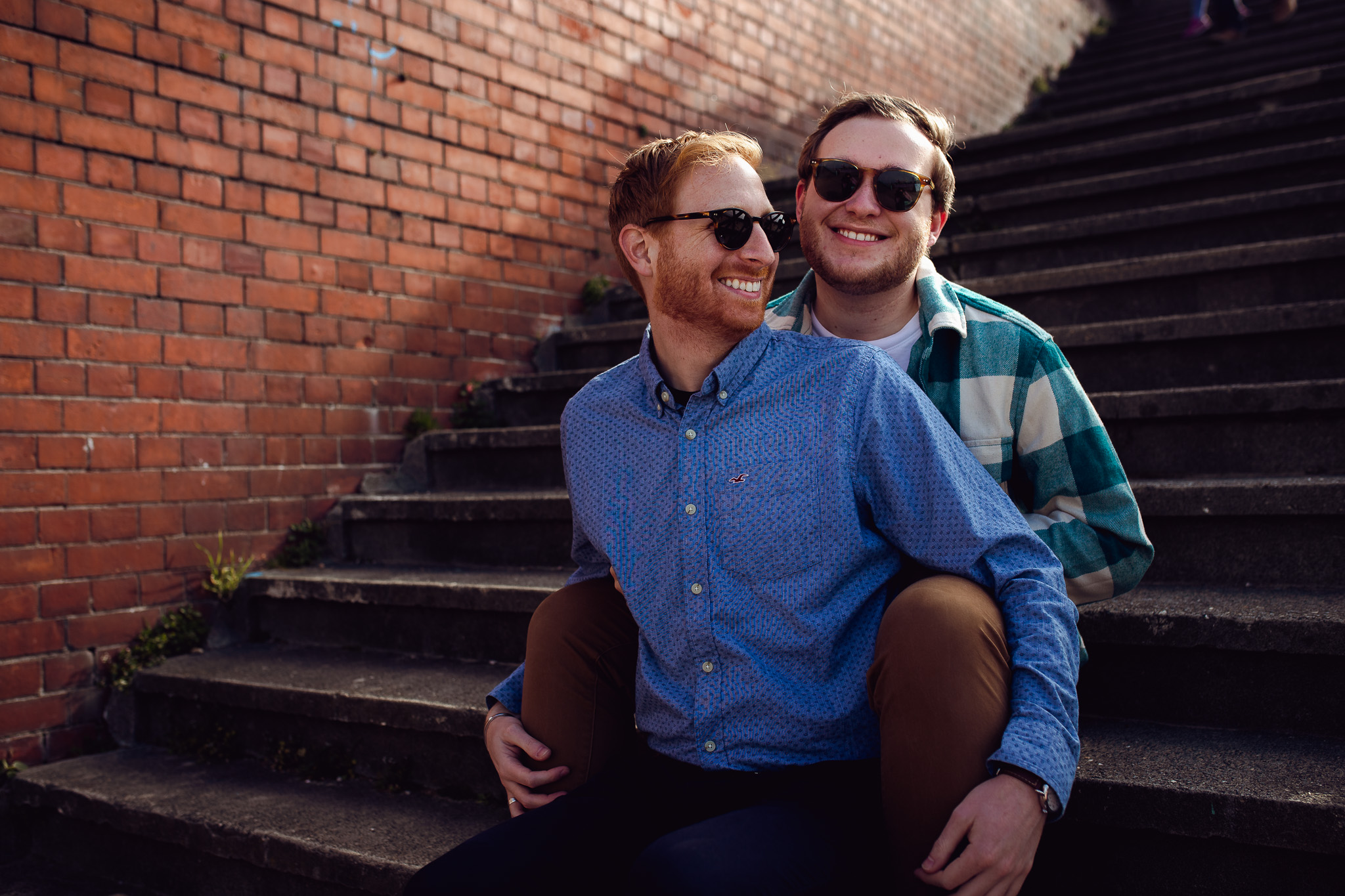 LGBTQ+ couple sitting on the stairs at Brighton Beach and smiling during their engagement shoot