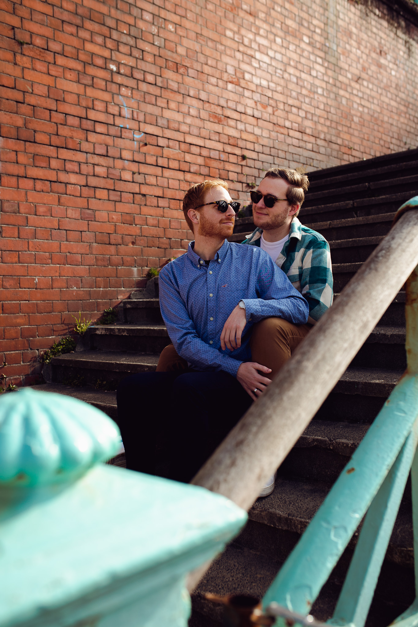 LGBTQ+ couple sit on the stairs at Brighton Beach during their engagement shoot