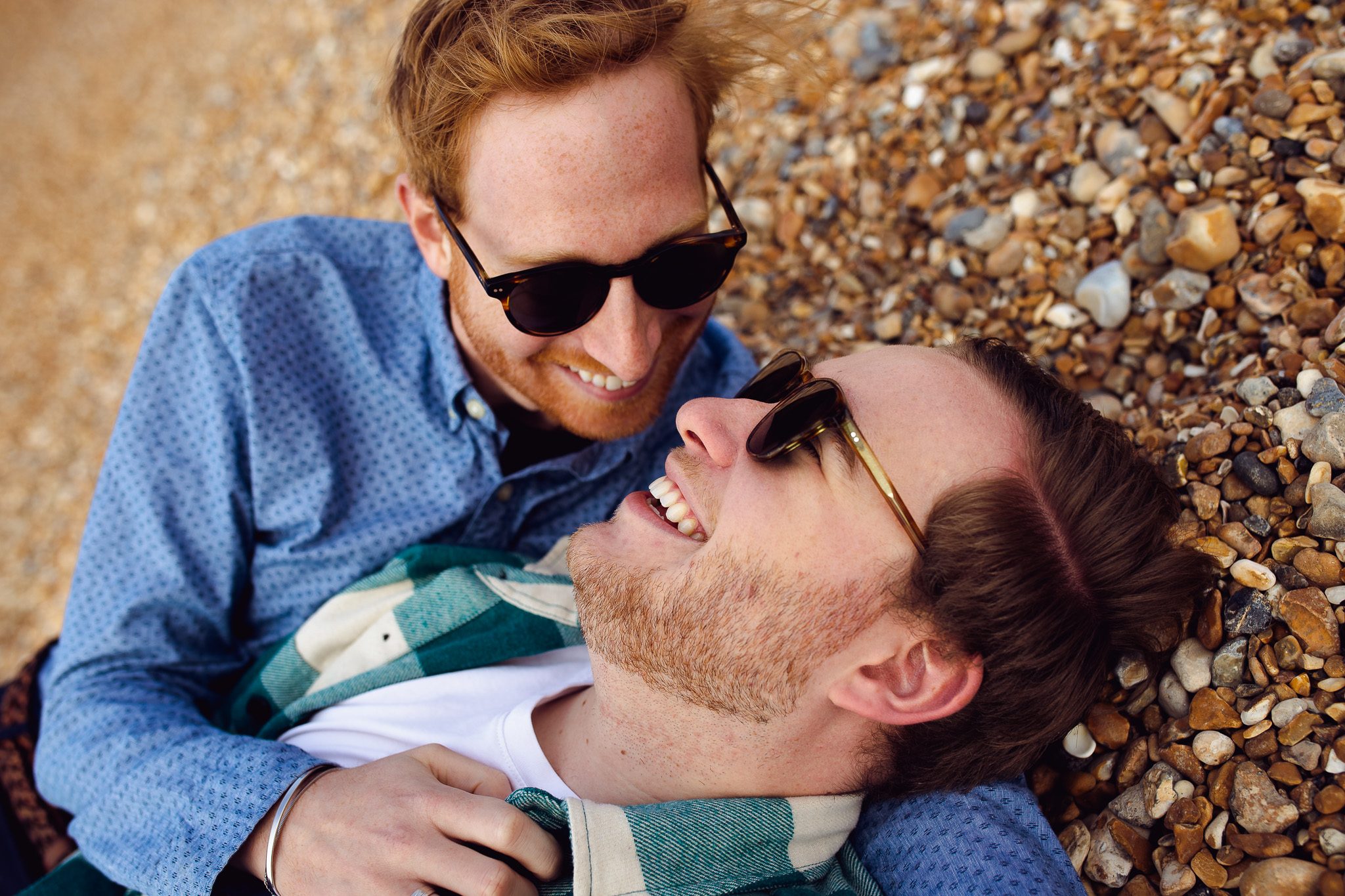 LGBTQ+ couple lie down on Brighton Beach and smile at each other during their engagement session