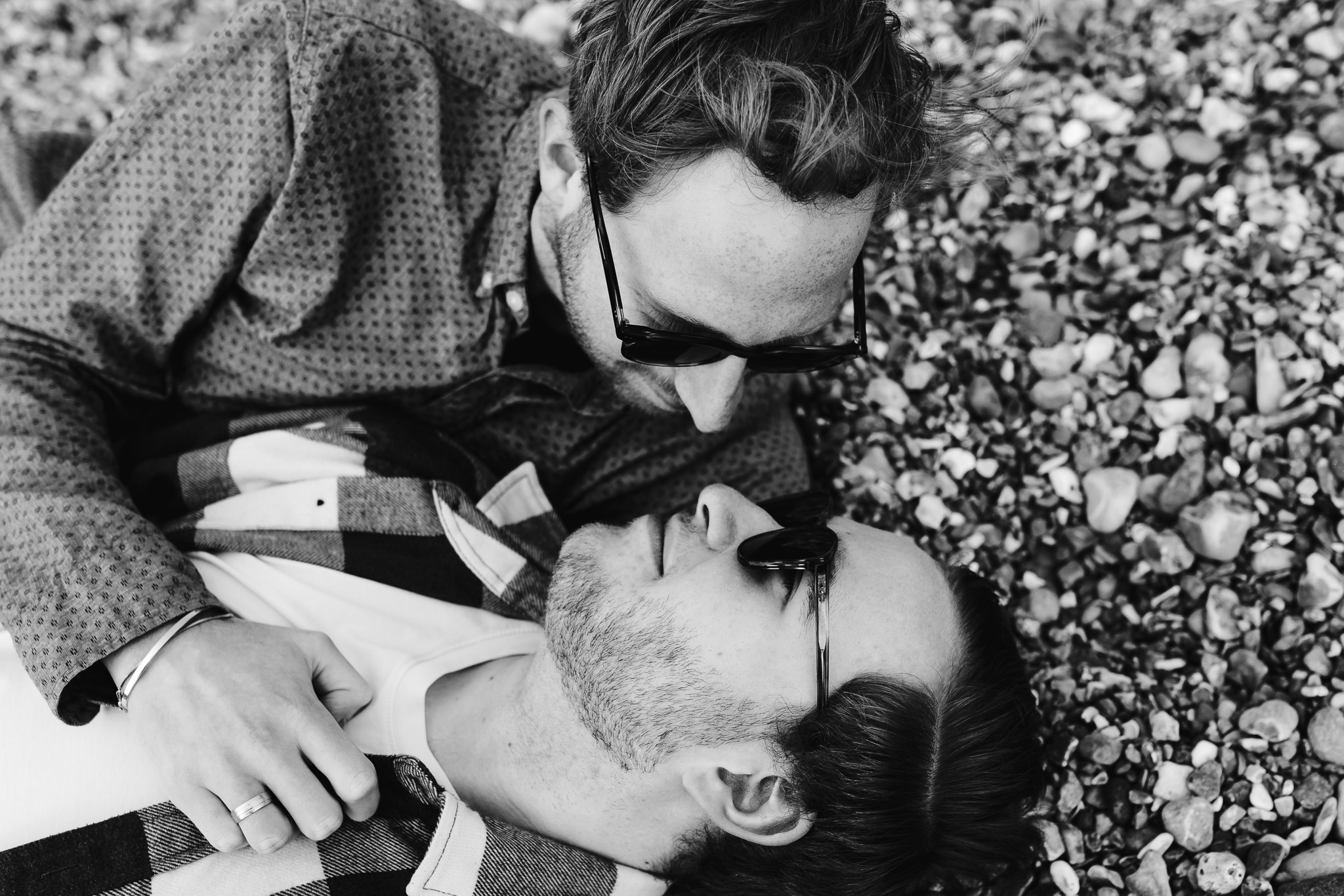 LGBTQ+ couple lying in the pebbles looking at each other during their engagement session