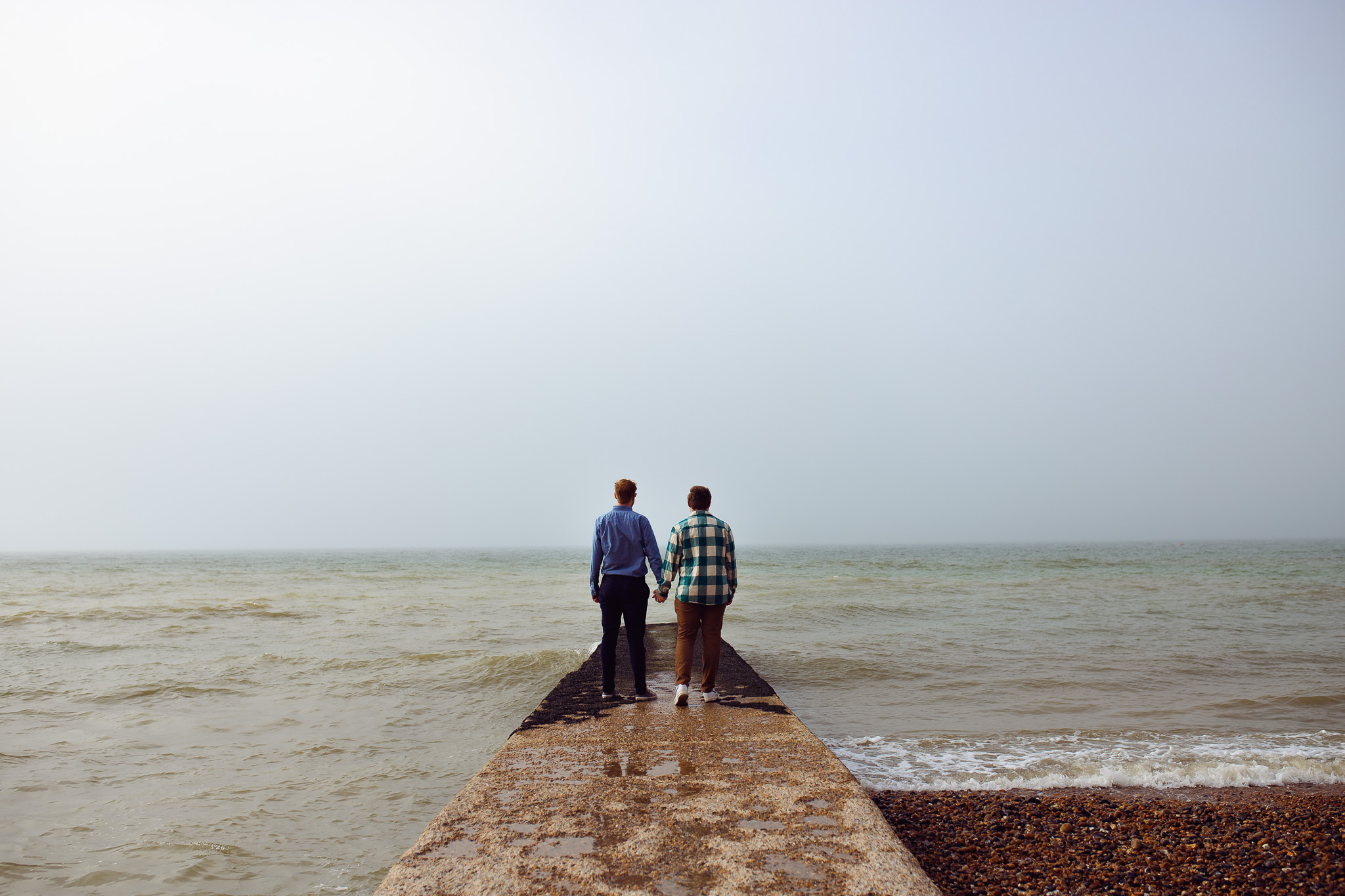 Brighton engagement session of an LGBTQ+ couple standing on a jetty looking out to the sea