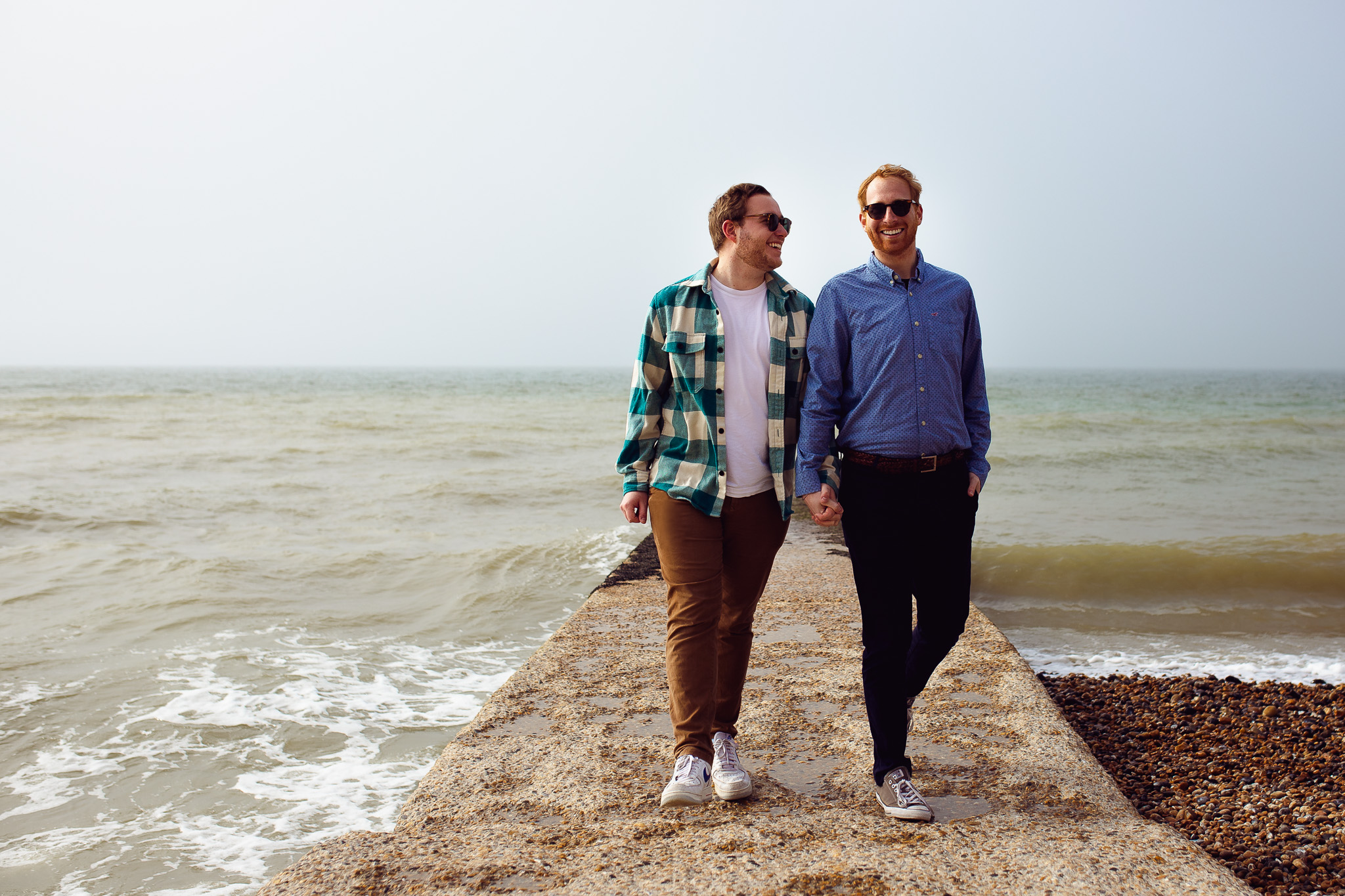 Brighton Beach engagement session of an LGBTQ+ couple holding hands and walking down the jetty