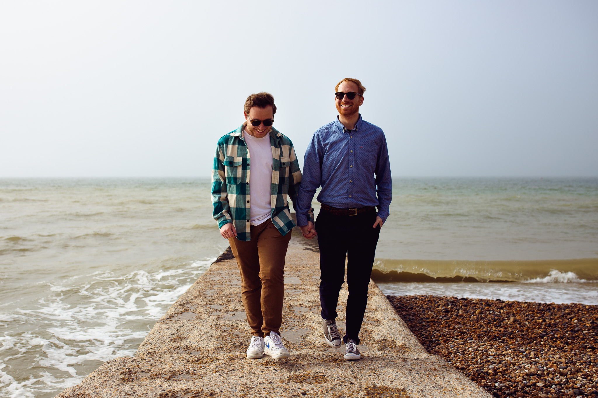 LGBTQ+ couple holding hands and walking down a jetty by the sea