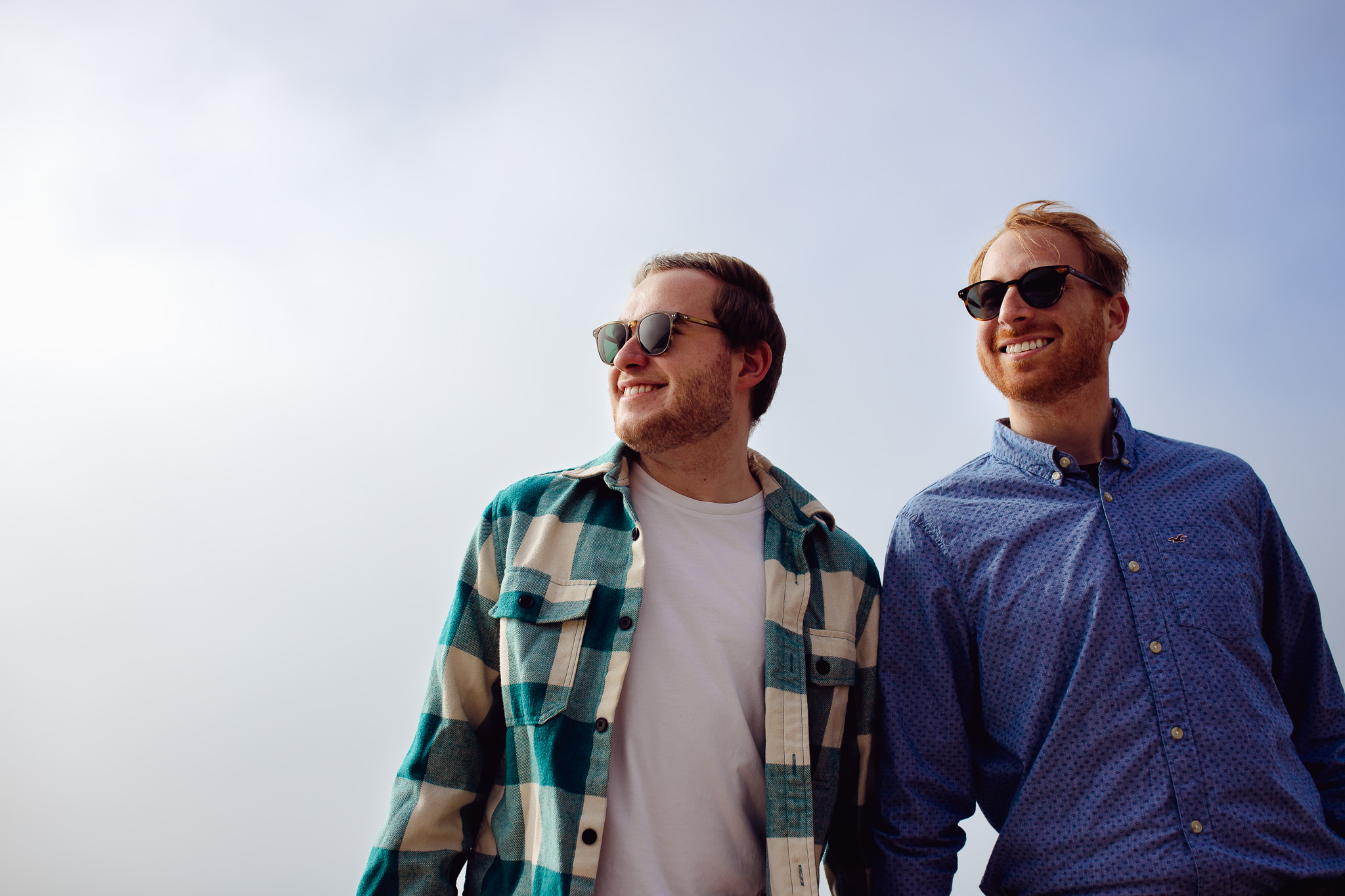 LGBTQ+ couple wearing sunglasses holding hands and smiling during their engagement shoot