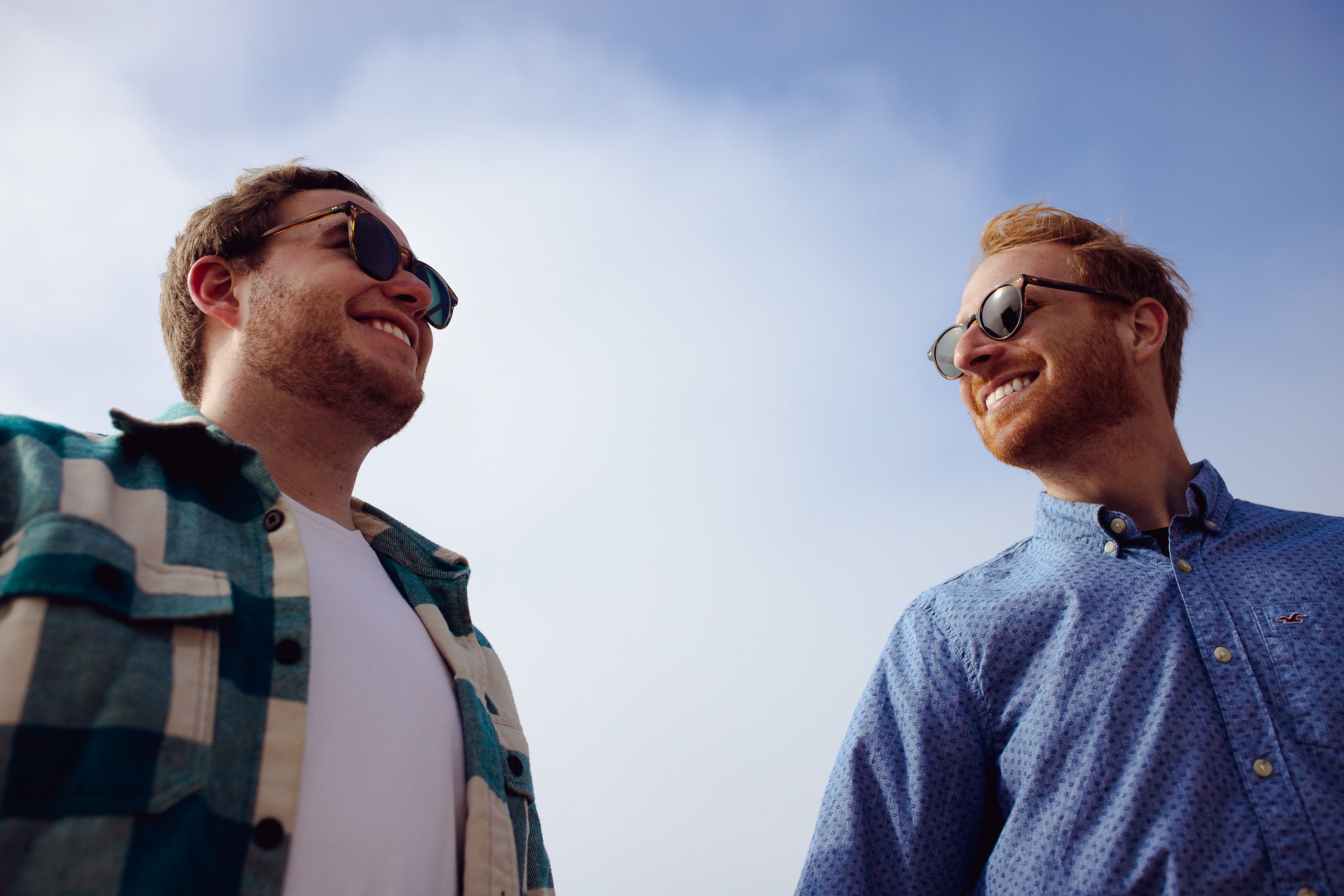 Engagement portrait of an LGBTQ+ couple wearing sunglasses and smiling at each other