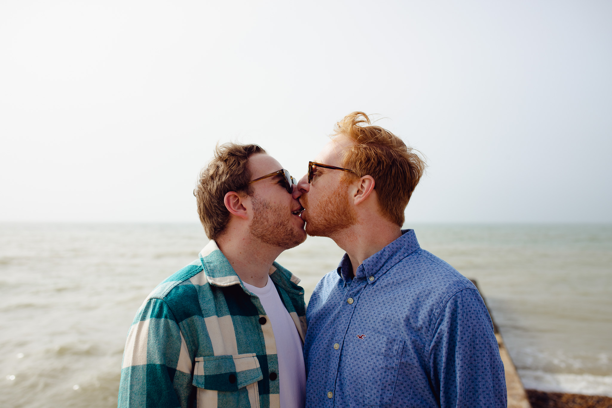 Engagement portrait of an LGBTQ+ couple kissing by the sea
