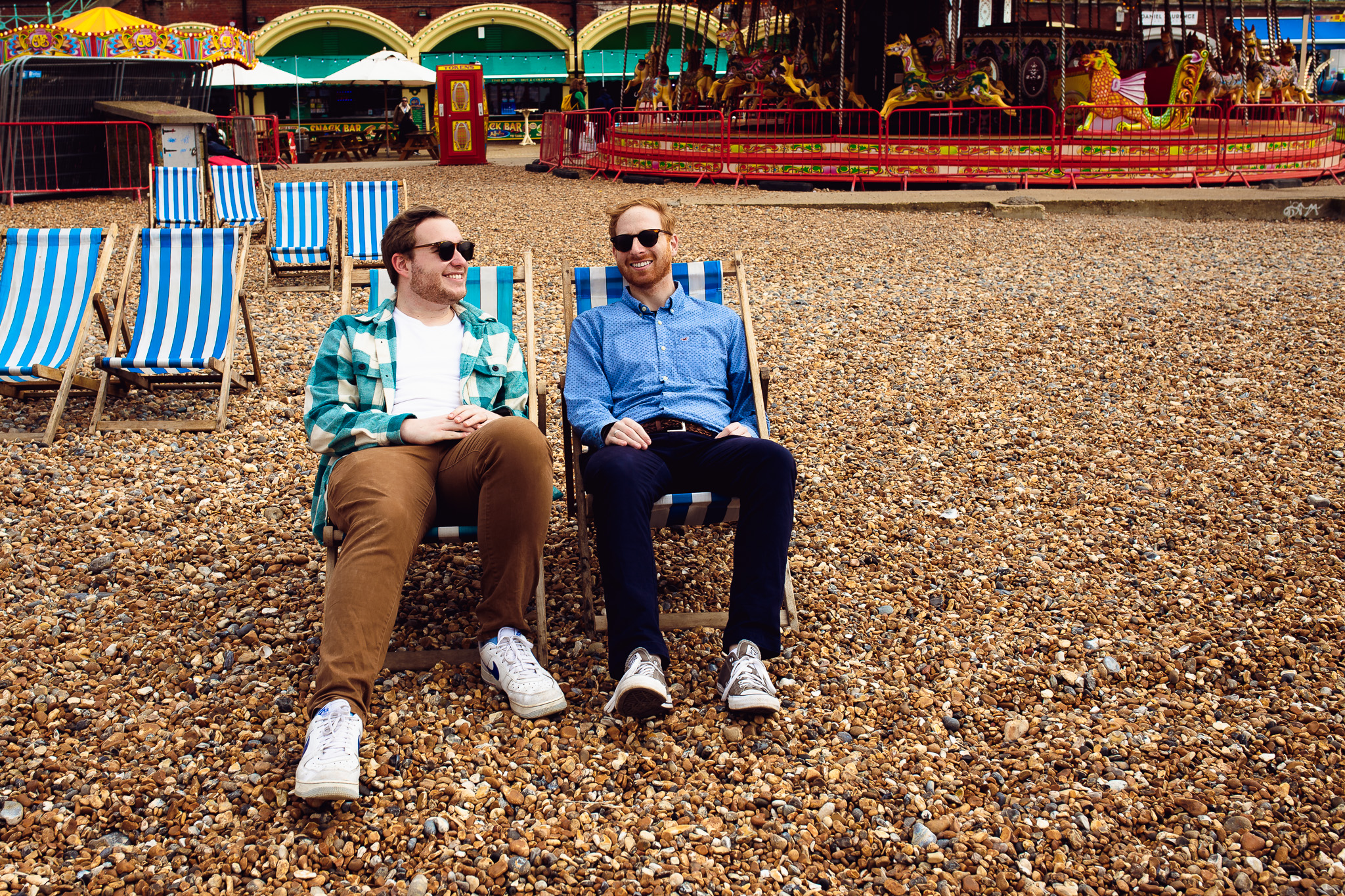 LGBTQ+ engagement session at Brighton Beach on the deck chairs near the carousel