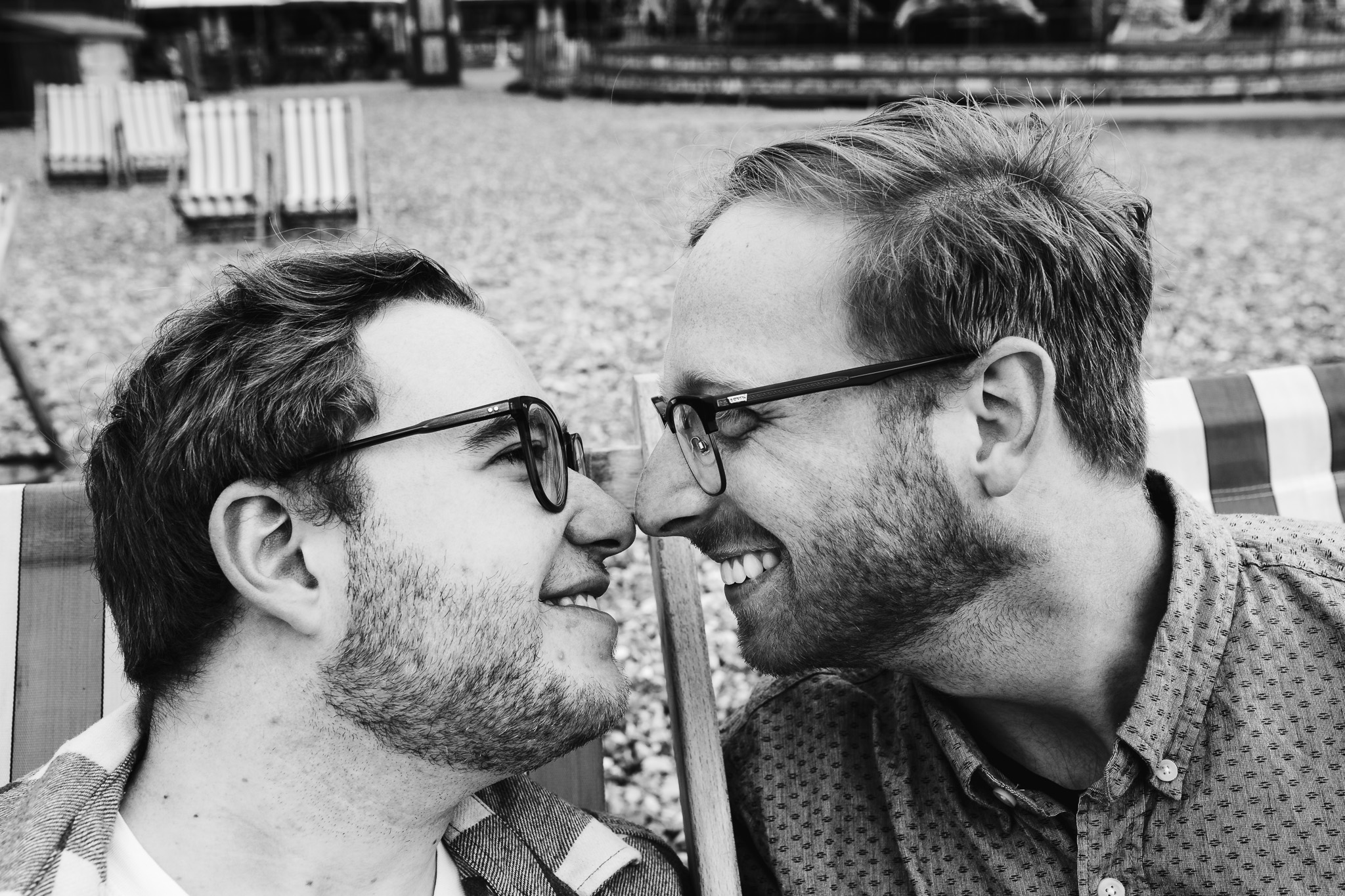 LGBTQ+ couple touching noses on deck chairs at Brighton beach during their engagement session