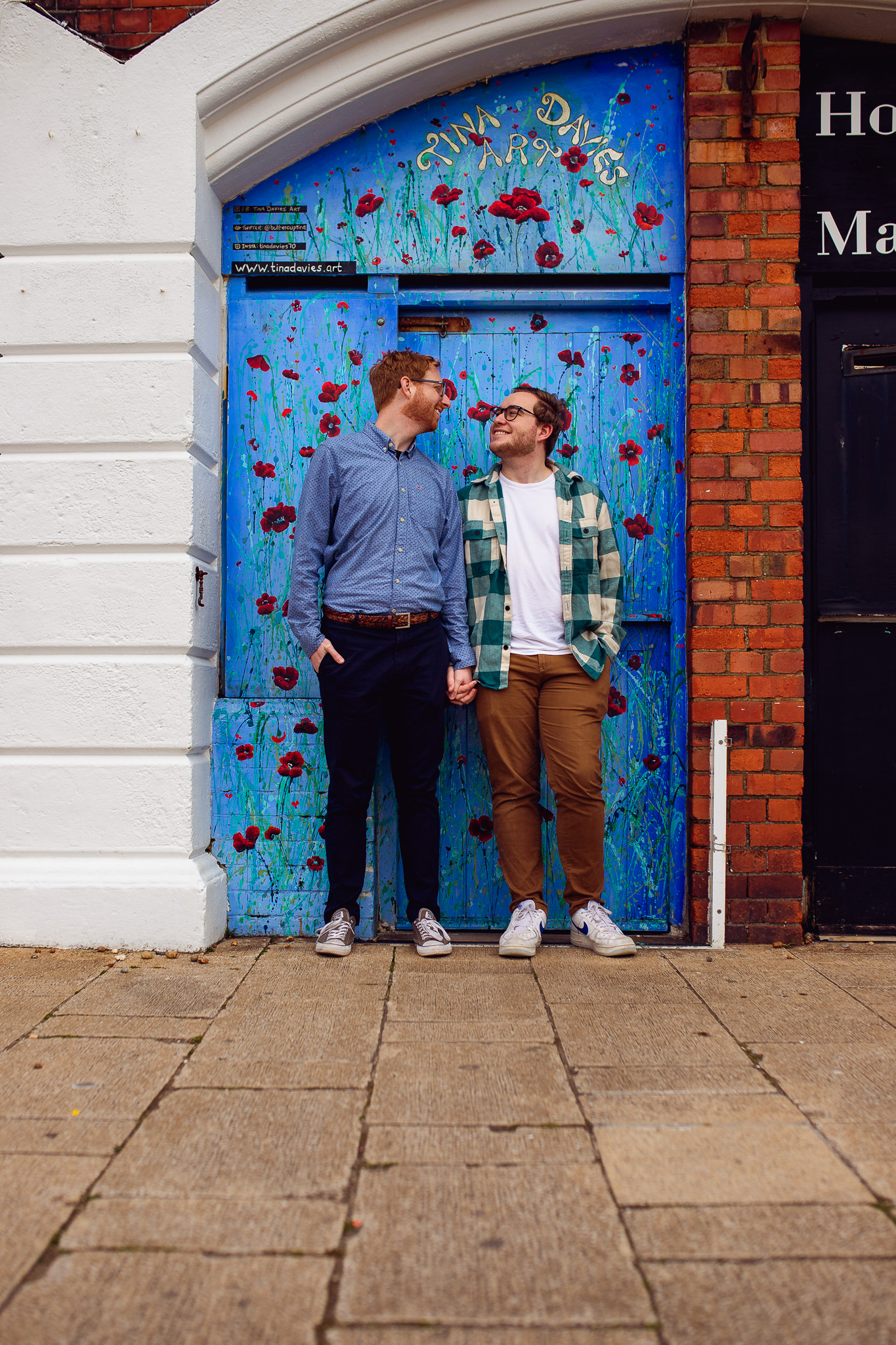 LGBTQ+ couple holding hands and looking at each other on Brighton promenade during their engagement shoot