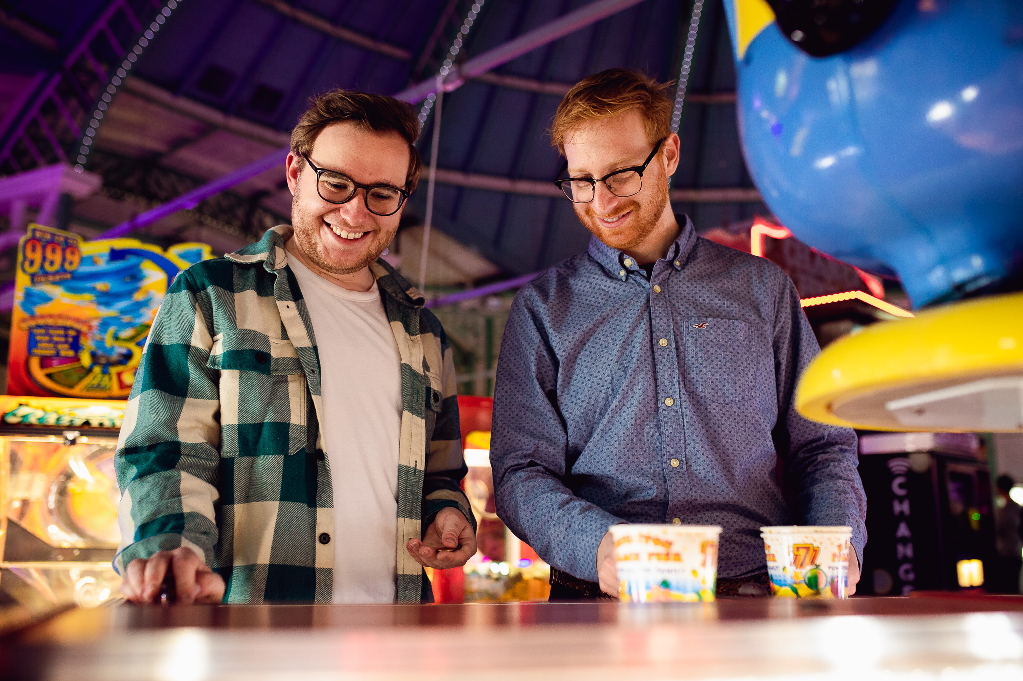 LGBTQ+ couple playing games at the arcade on Brighton Pier and smiling during their engagement session