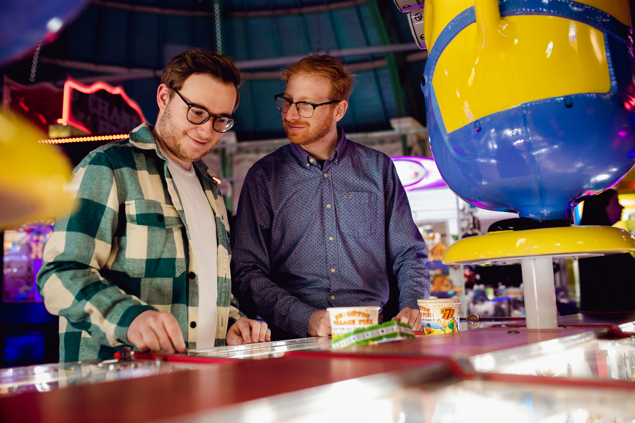 LGBTQ+ couple looking at each other whilst playing slots at the arcade on Brighton pier