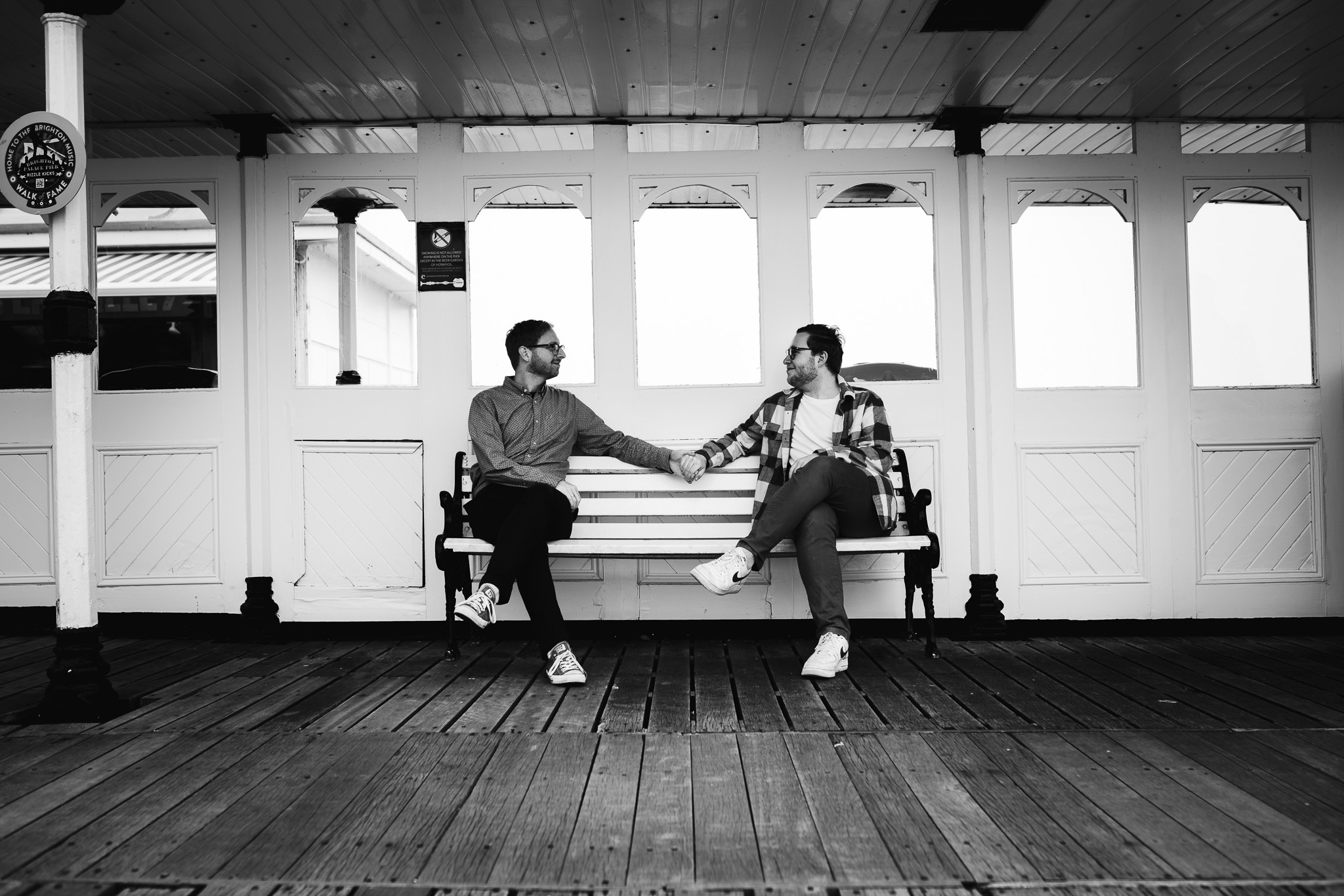 LGBTQ+ couple sitting on bench at Brighton pier holding hands during a engagement session