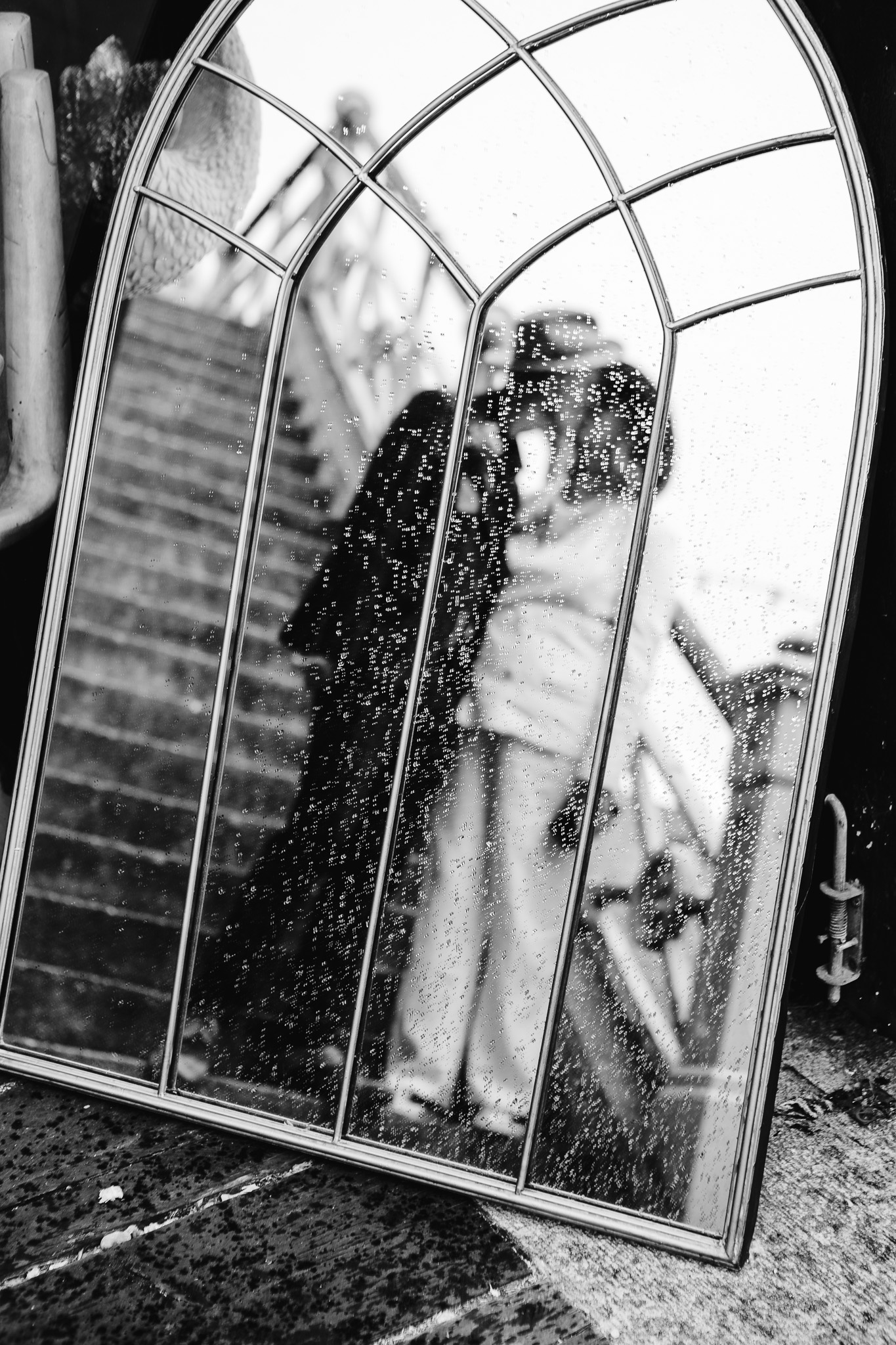 Bride and grooms kissing reflection in a intricate mirror covered in rain drops.