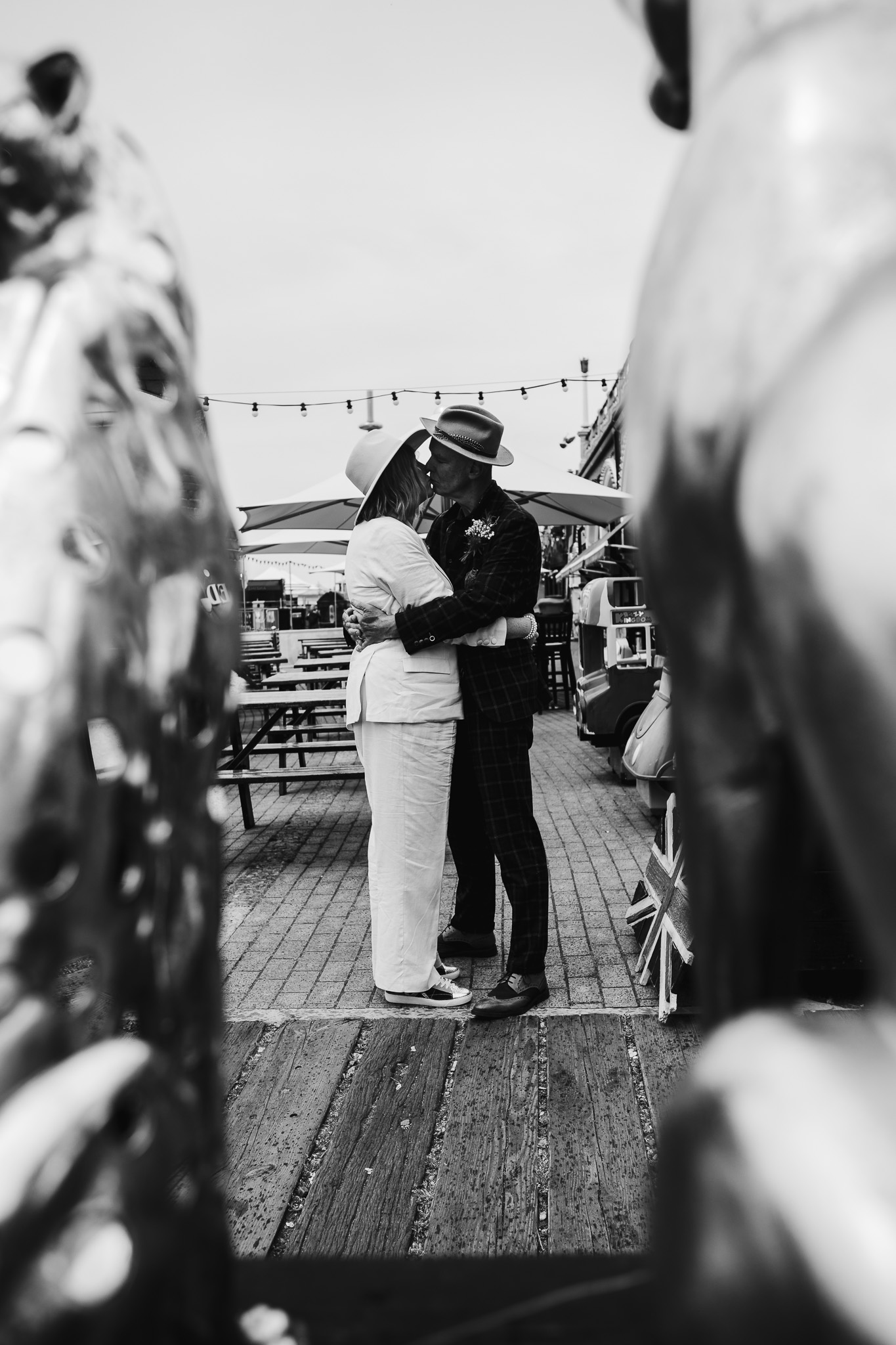 A shot through shop trinkets of Mary and Mike embracing during a wedding couple portrait session near Brighton beach.