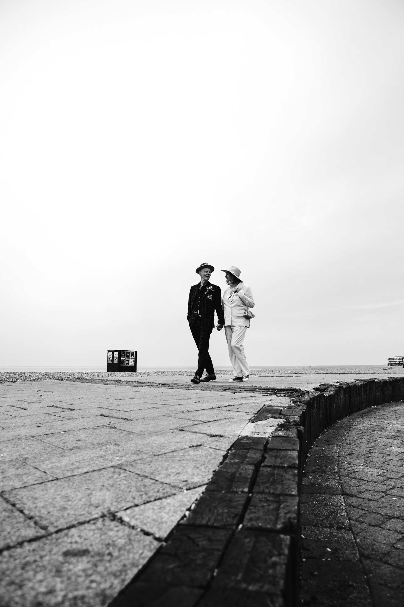 Mary and Mike walk down Brighton beach holding hands looking at each other during their couple portrait session.