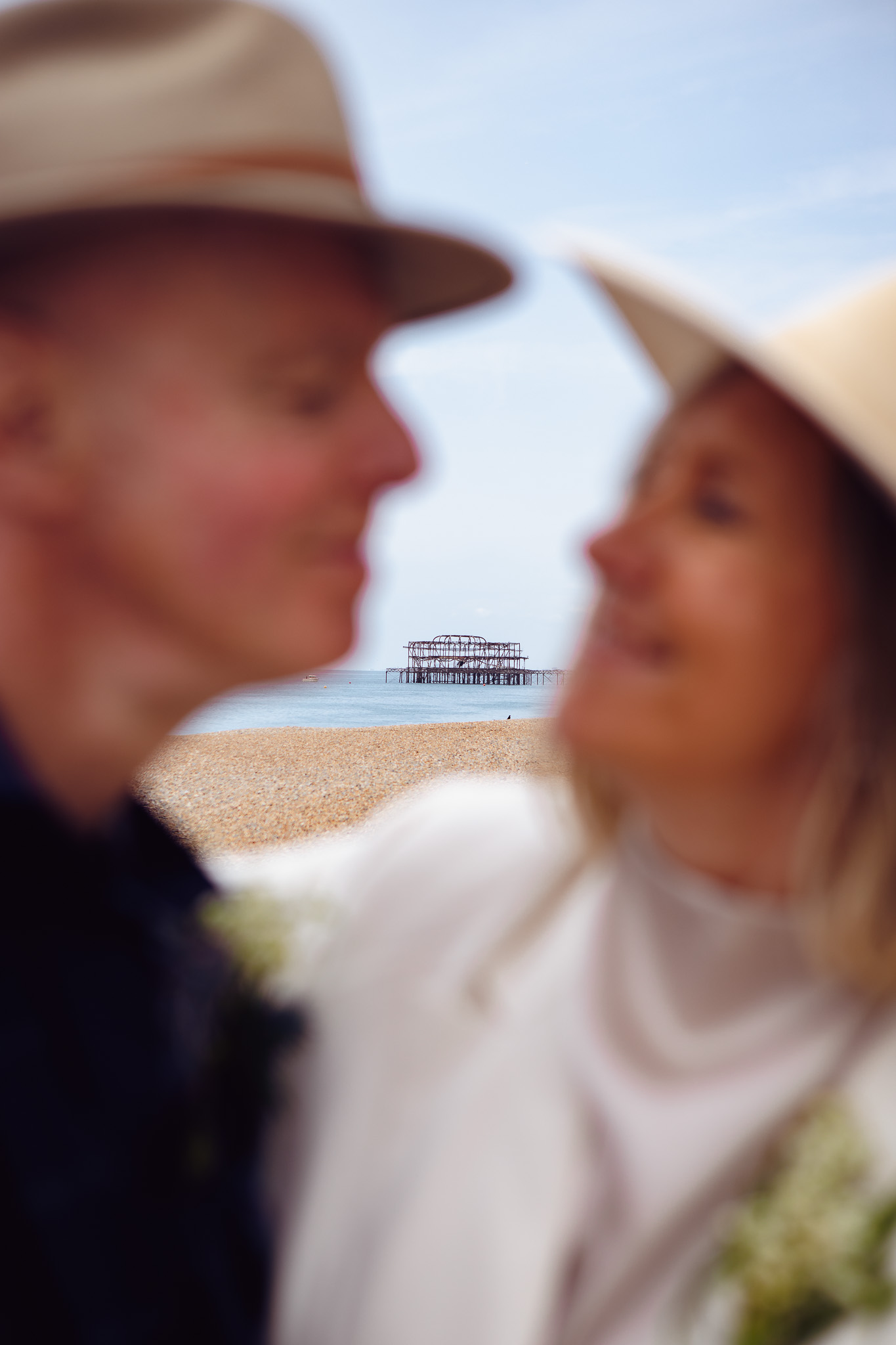 Brighton West Pier in the background of a couple in fedoras during their wedding portrait session.