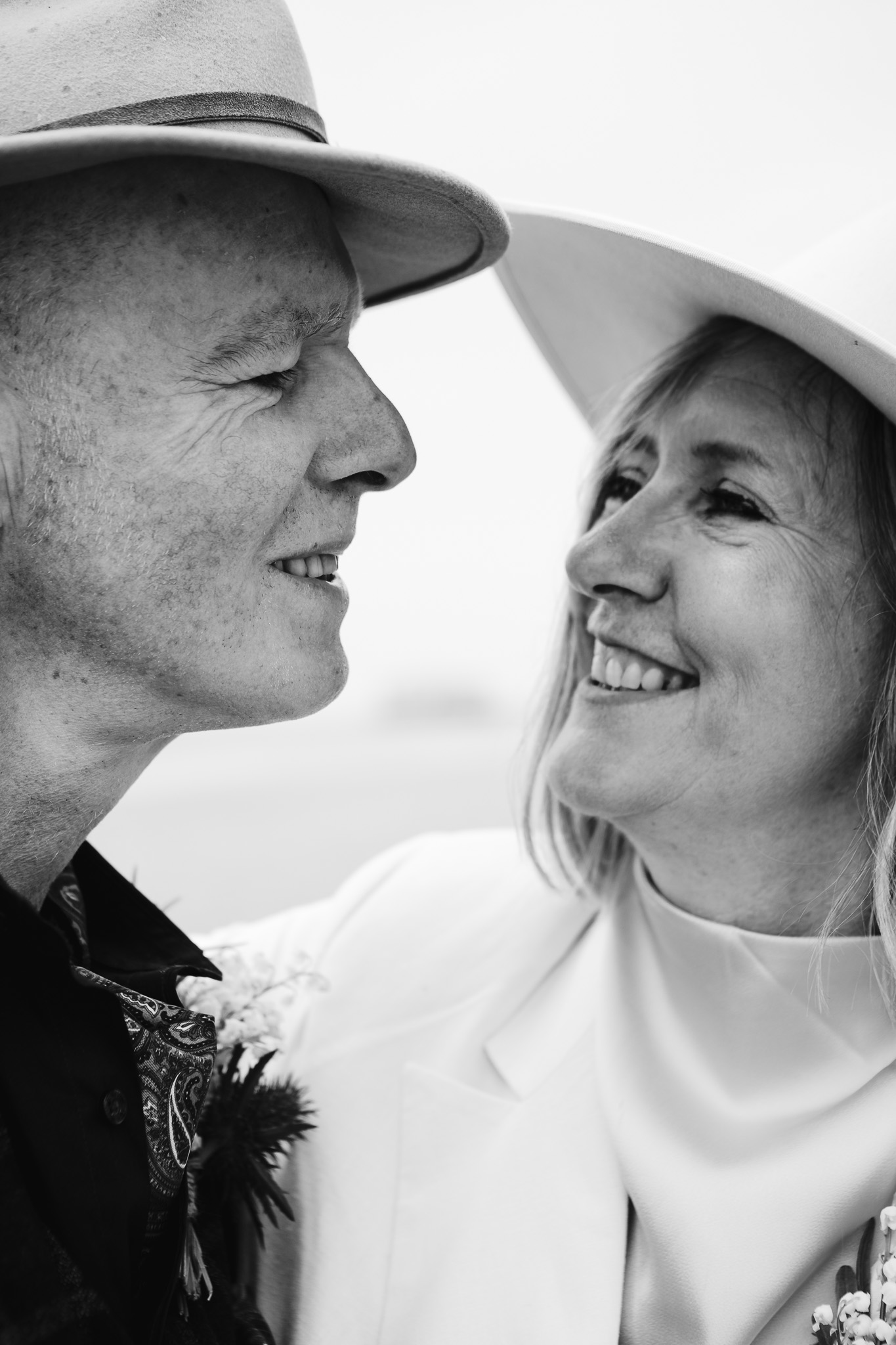 Bride and groom wearing fedoras look at each other and smile during their couple portrait session.