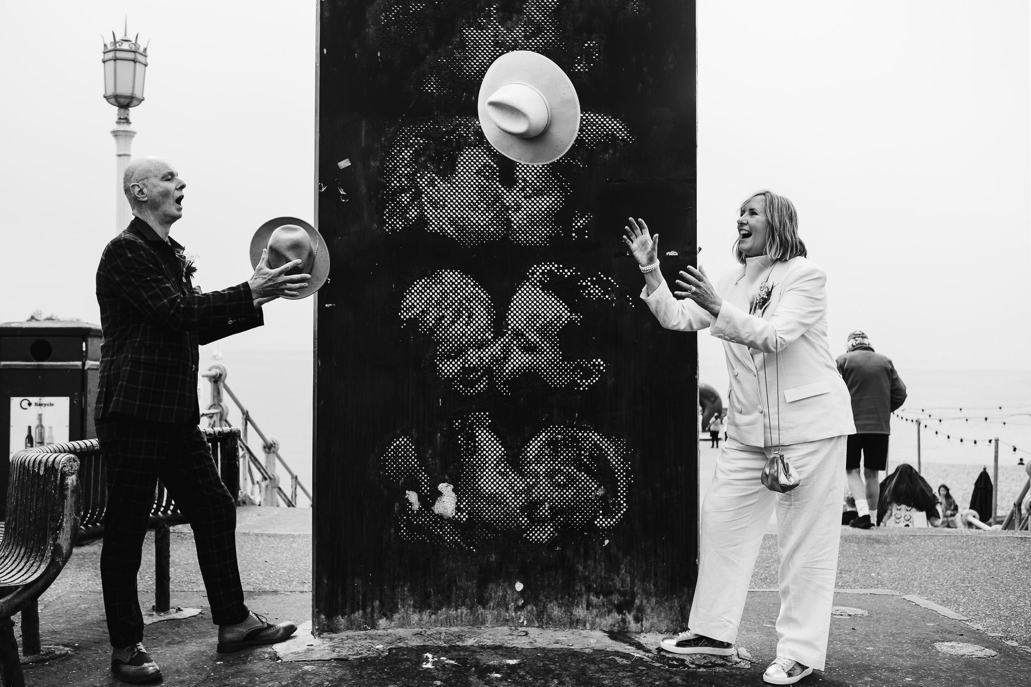 Mary and Mike throw their fedoras to each other during a couple portrait session in front of the kissing statue on Brighton beach.