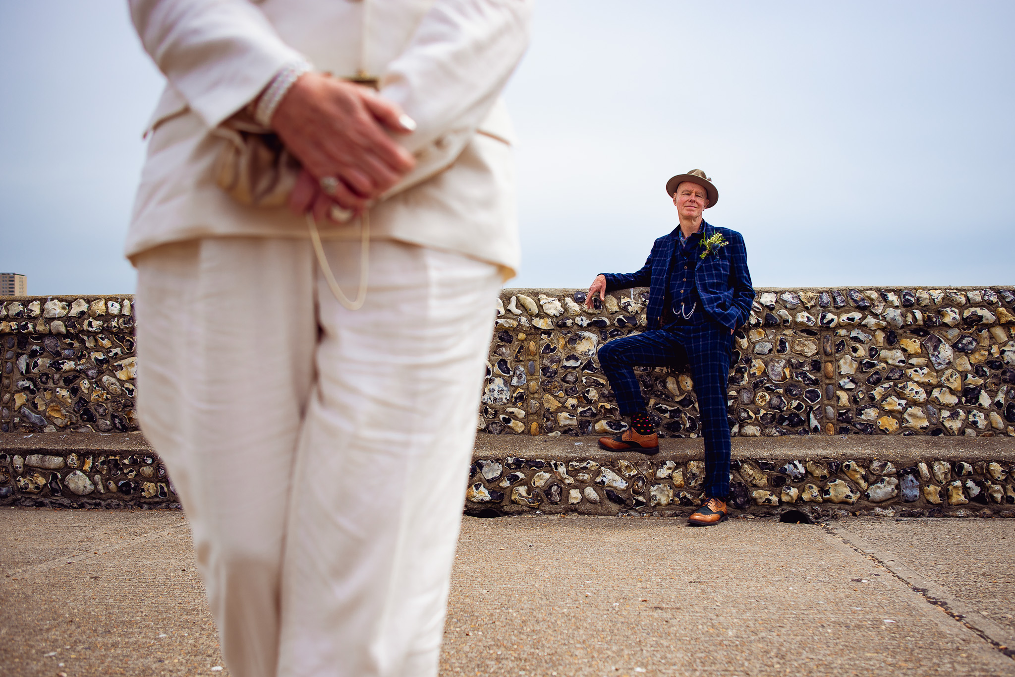 Mike poses in front of a stone wall near Brighton pier whilst Mary walks towards the photographer.