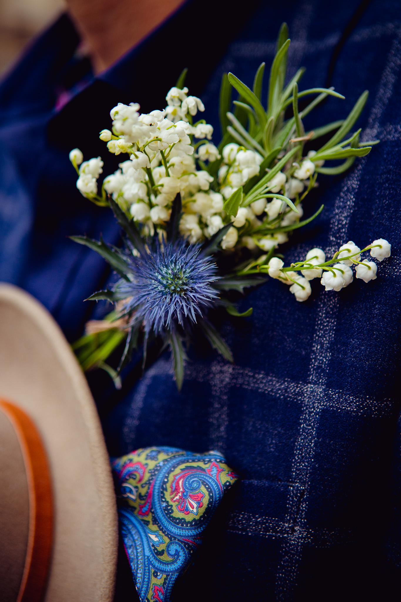 Close-up of the groom's white and blue flower lapel in his blue suit buttonhole.