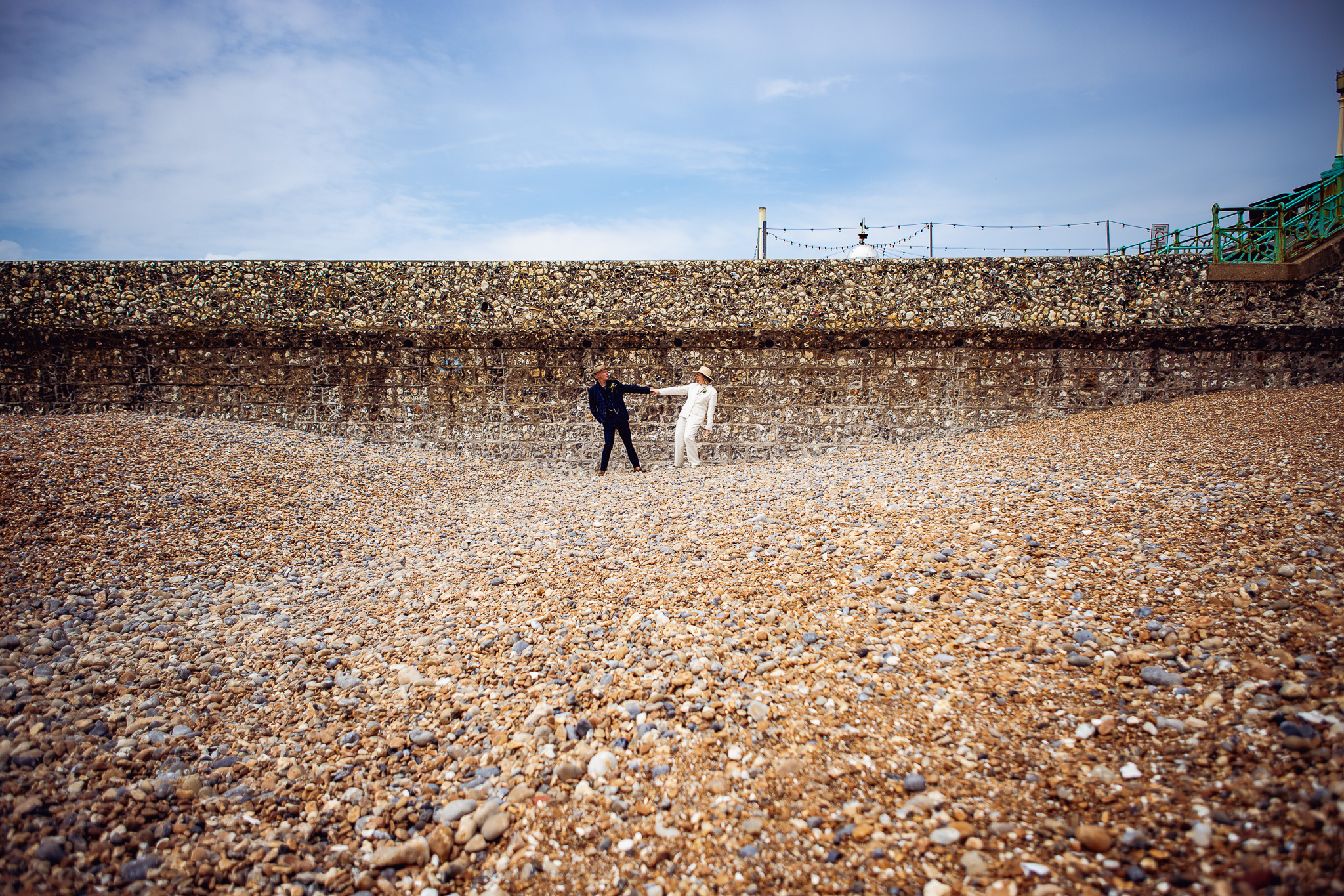 Mary and Mike hold hands and lean back whilst posing for couple portraits on Brighton beach.