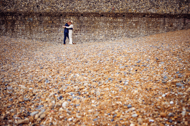 Mary and Mike embrace on Brighton beach as they pose for their wedding couple portrait session.