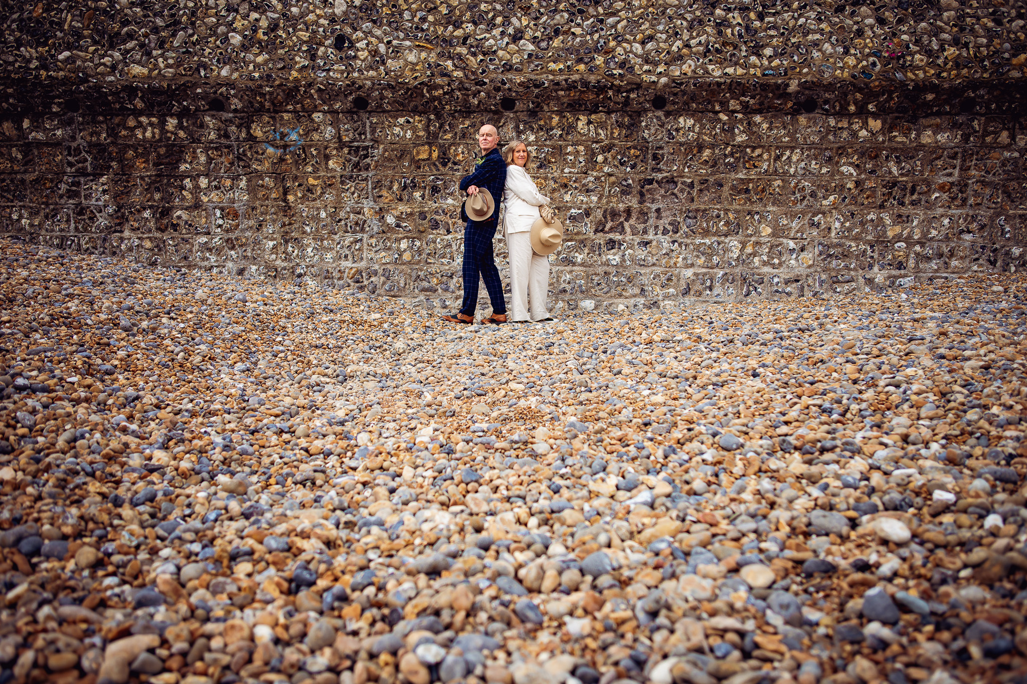 Mary and Mike pose back to back holding their fedoras during their couple portrait session on Brighton beach.