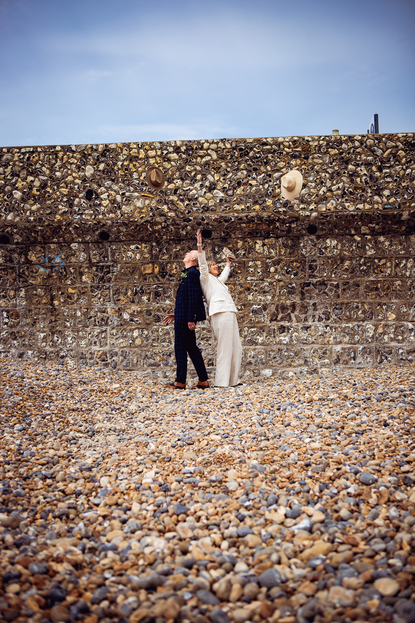 Mike and Mary throw their fedoras in the air during their wedding couple portrait session on Brighton beach.
