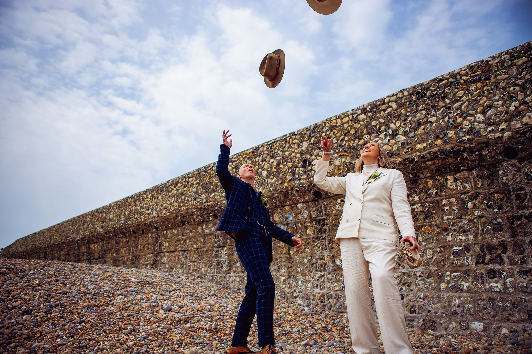 Mary and Mike throw their fedoras in the air during their wedding couple portrait session on Brighton beach.