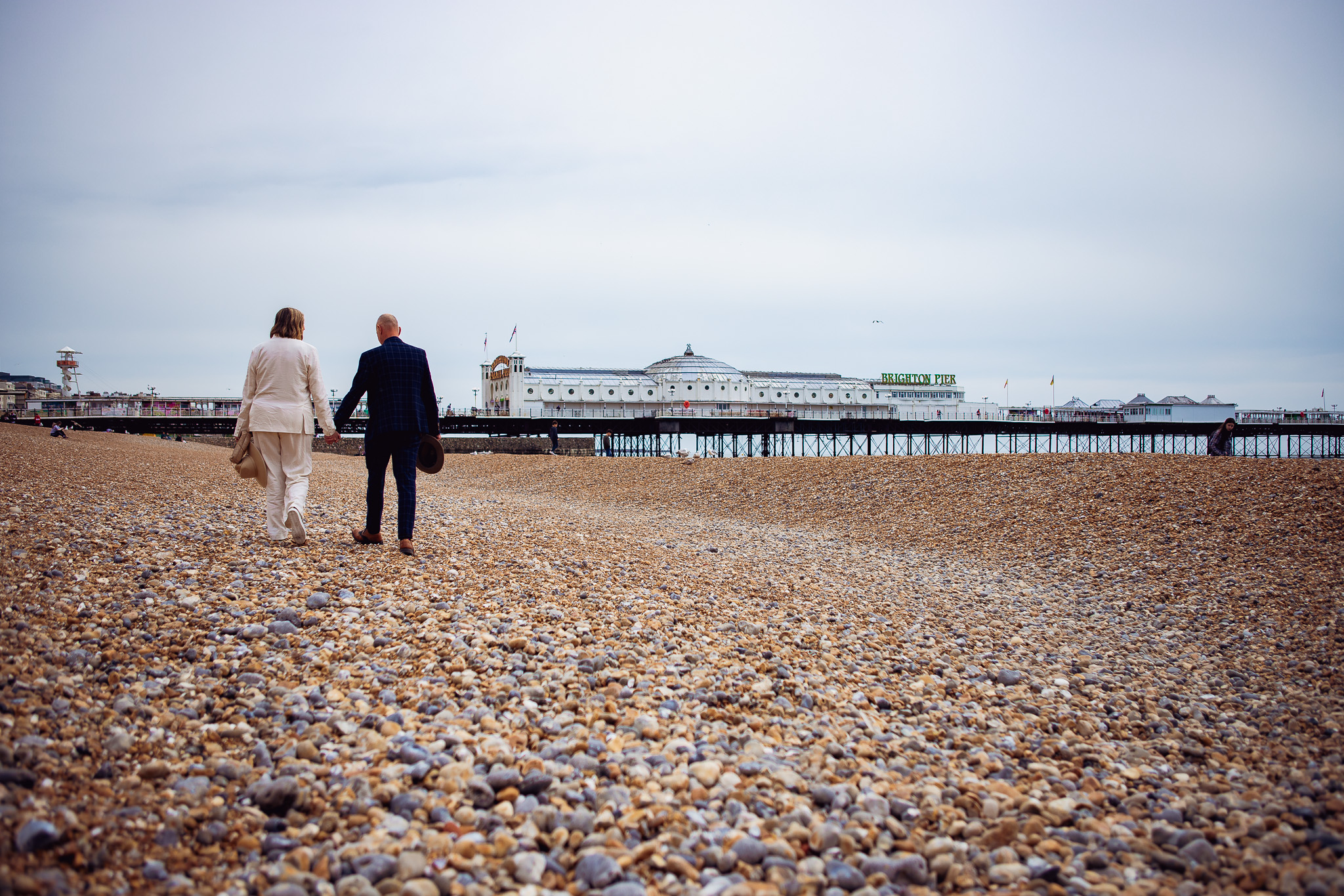 Mary and Mike walk down the beach near Brighton Pier during their wedding couple portraits.