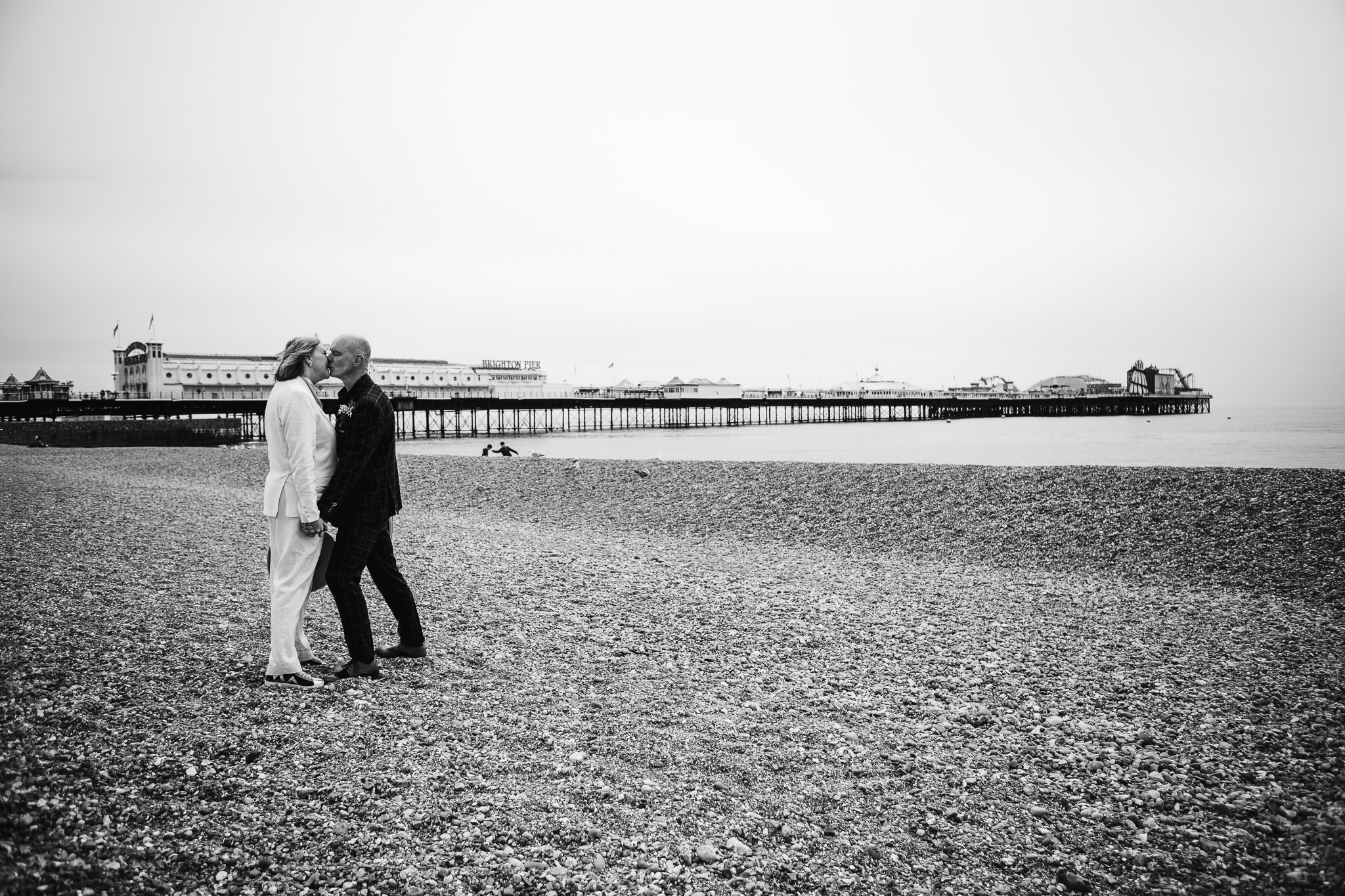 Mary and Mike kiss near Brighton Pier on the beach during their wedding couple portraits.
