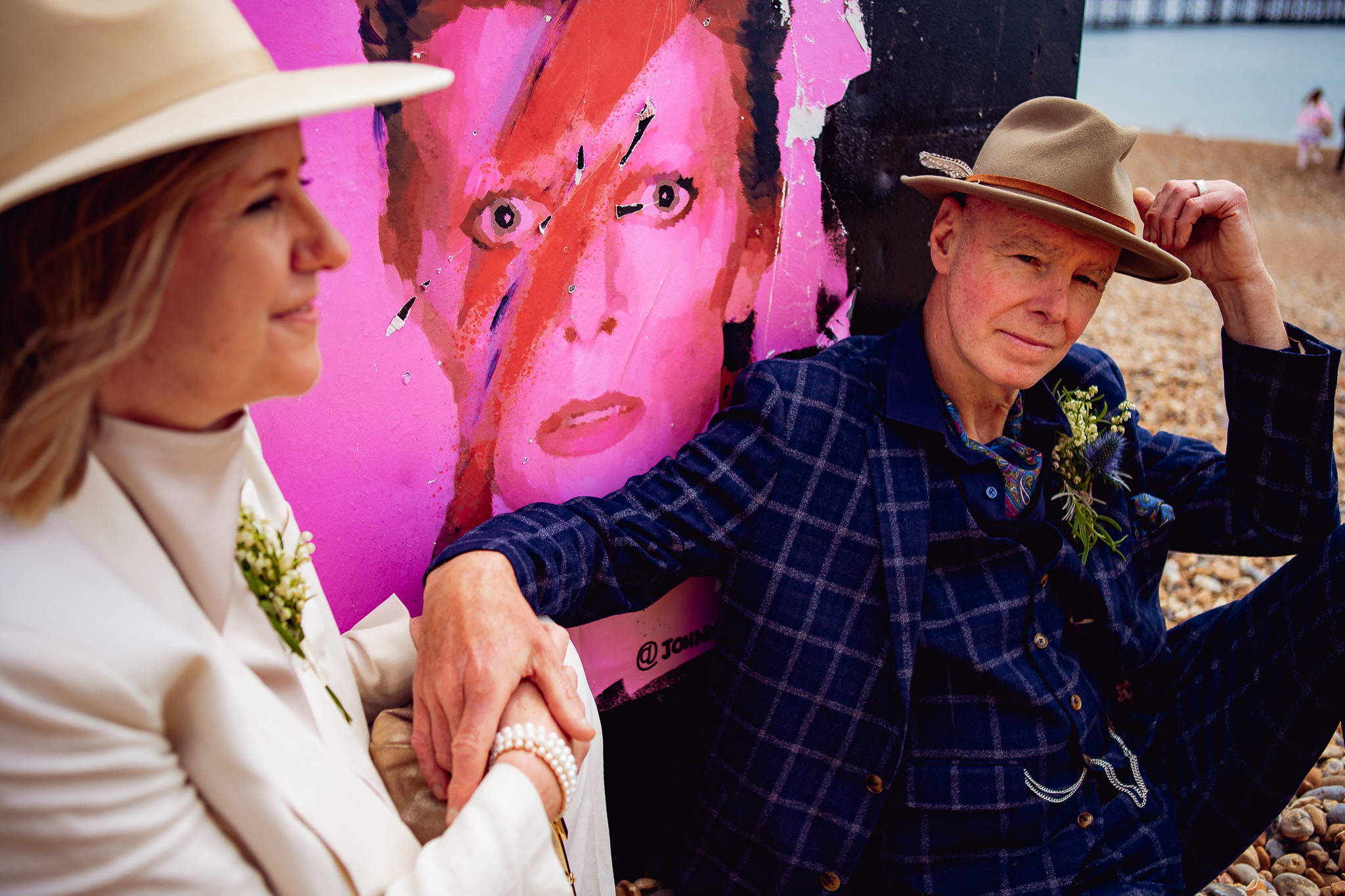 Mary and Mike posing with a poster of David Bowie during their wedding couple portraits on Brighton beach.