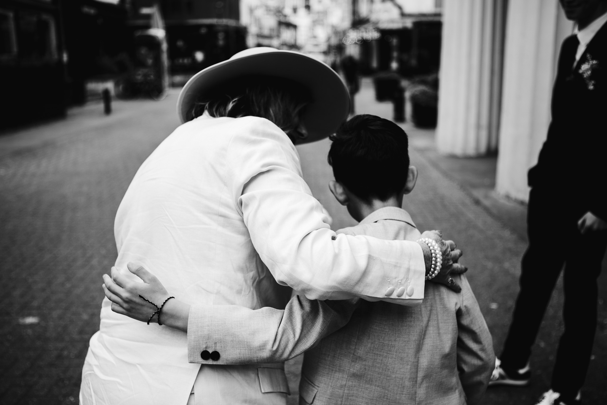 Bride and a little boy put arms around each other's backs in greeting outside Brighton Town Hall.